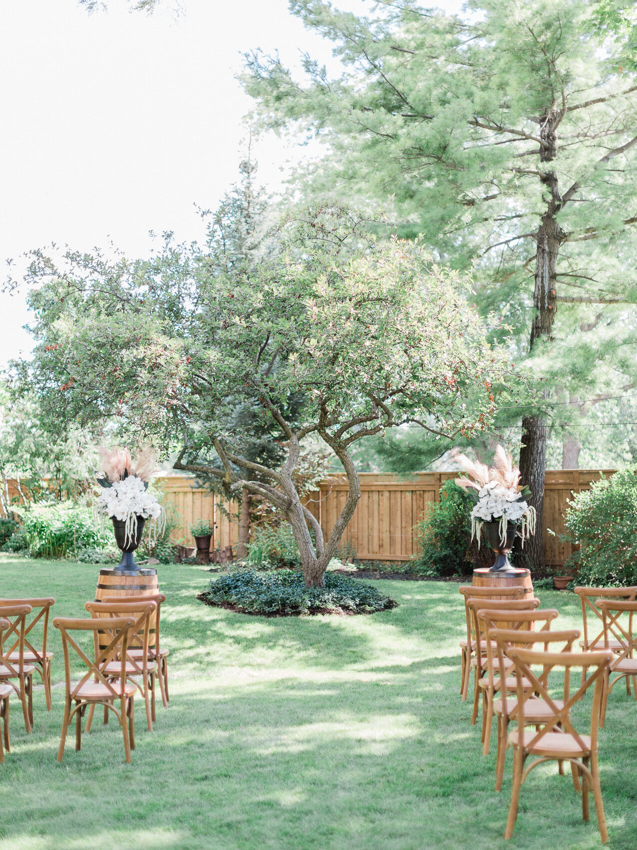 a backyard wedding set up with harvest chairs and an apple tree