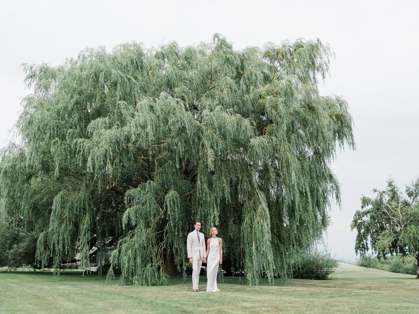 a couple pose naturally in front of a giant tree for their wedding photographs