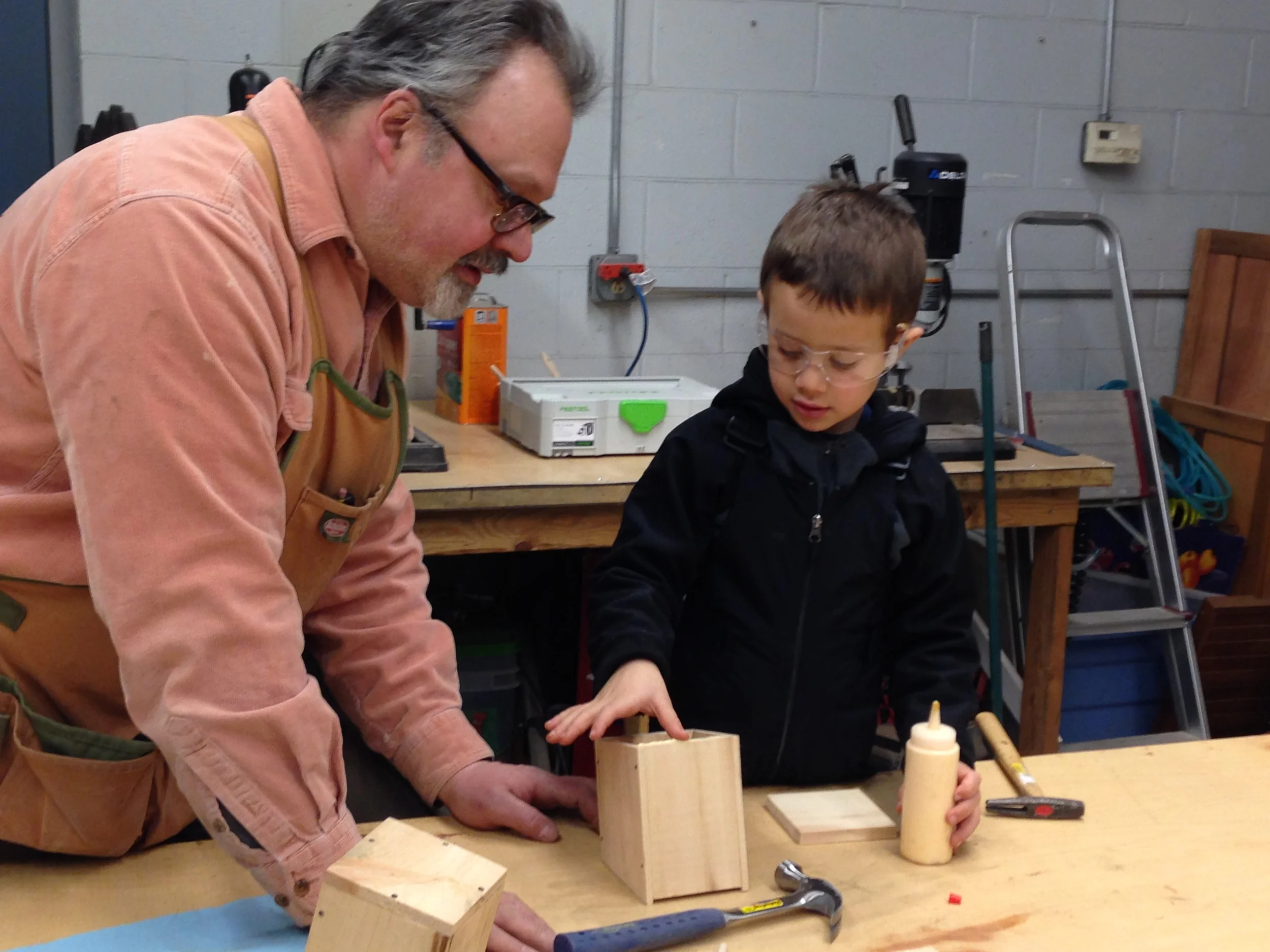 Silas spreads glue on the end walls of his birdhouse before nailing the floor into place.