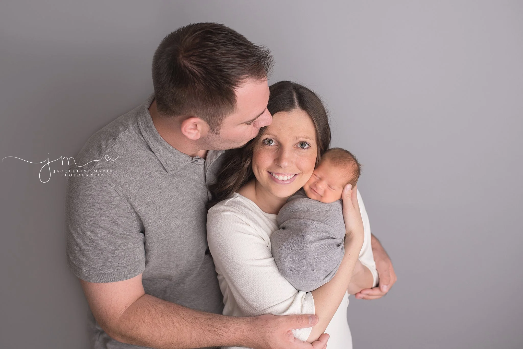 Columbus Ohio newborn photographer features portrait of parents holding baby with newborn smiling and father kissing mother