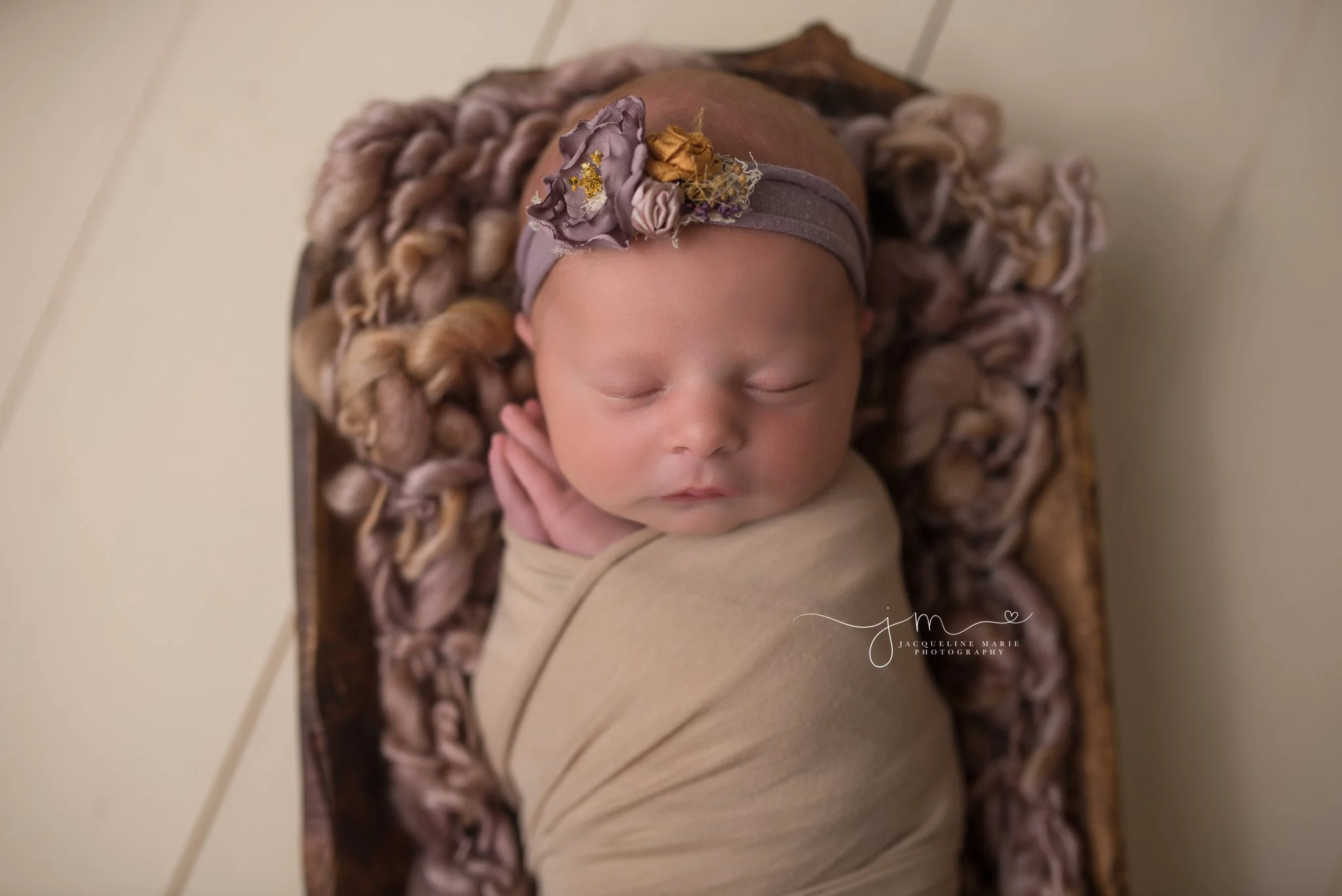 Columbus Ohio newborn baby girl is swaddled in tan wrap with purple headband for portrait session at Jacqueline Marie Photography