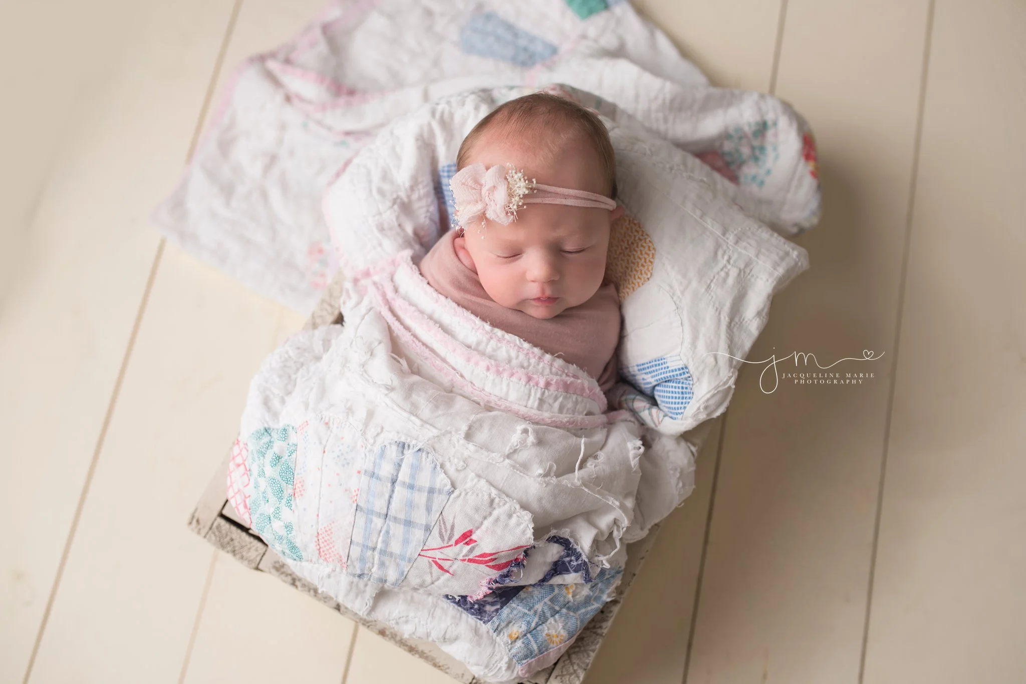 Newborn photography portrait by Jacqueline Marie Photography features baby wrapped in a vintage quilt with pink headband in Columbus Ohio