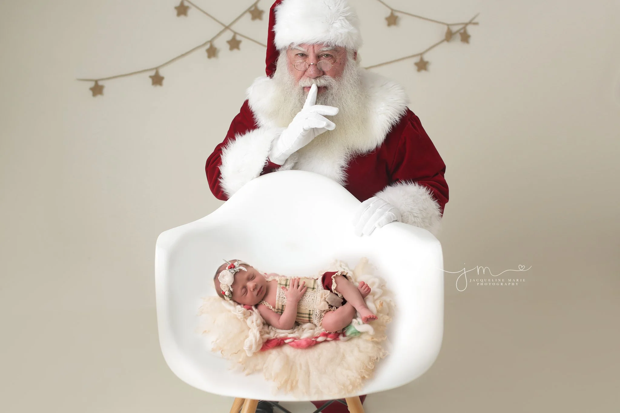 Columbus Ohio newborn baby girl sleeps in chair while Santa whispers behind her for newborn portrait session at Jacqueline Marie Photography studio