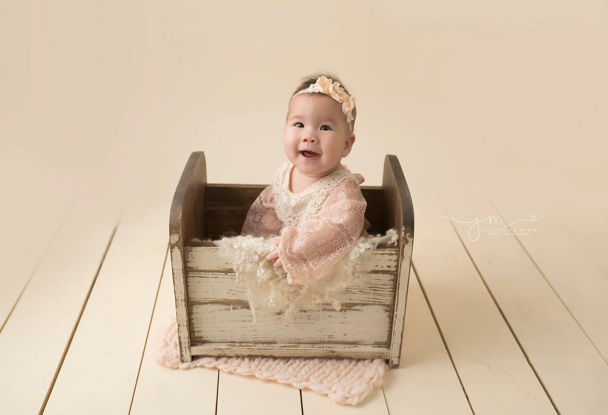 6 month old baby girl from new albany ohio wears pink romper while sitting in cream wood bed for milestone pictures at jacqueline marie photography