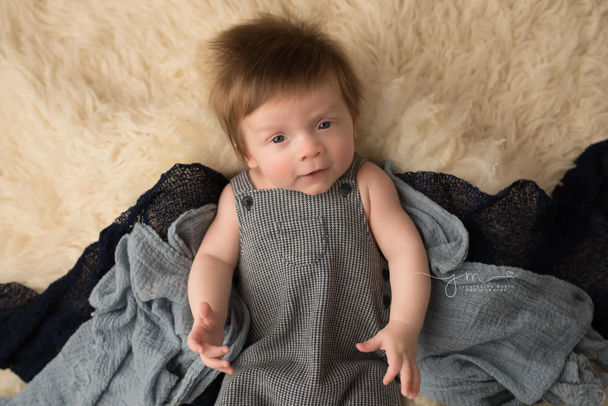 3 month old baby boy smiles with hands stretched out wearing janie and jack romper for milestone baby pictures in columbus ohio by jacqueline marie photography