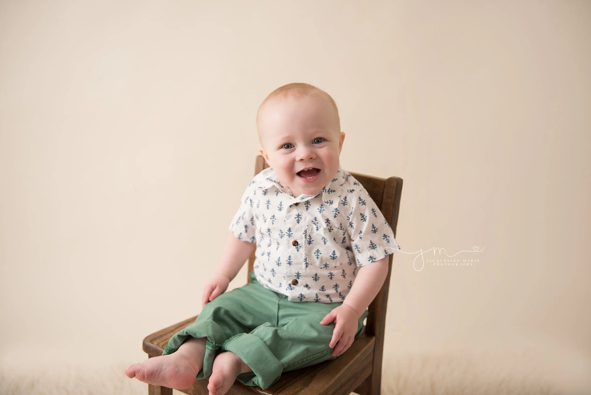 columbus ohio 1 year old smiles while wearing green pants and sitting on wooden chair for first birthday pictures