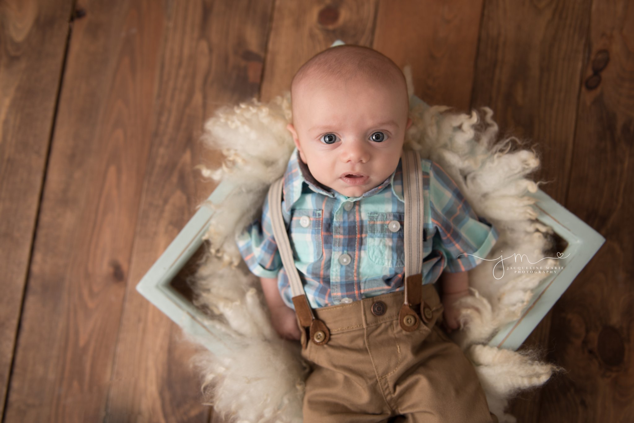 3 month old baby boy with blue eyes is posed in blue wooden prop on wood floor in columbus ohio at jacqueline marie photography studio