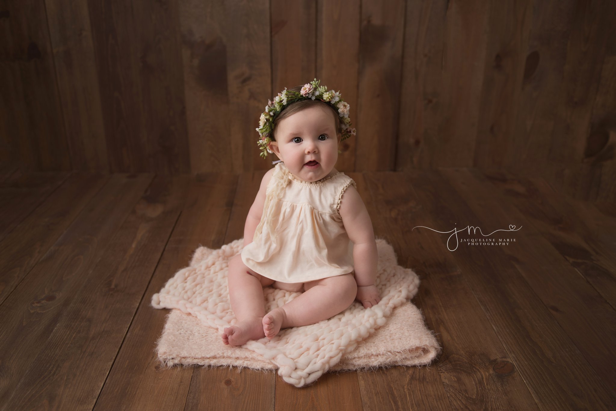 columbus ohio 6 month old baby girl sits on wood floor and wears floral crown for milestone baby pictures at jacqueline marie photography studio