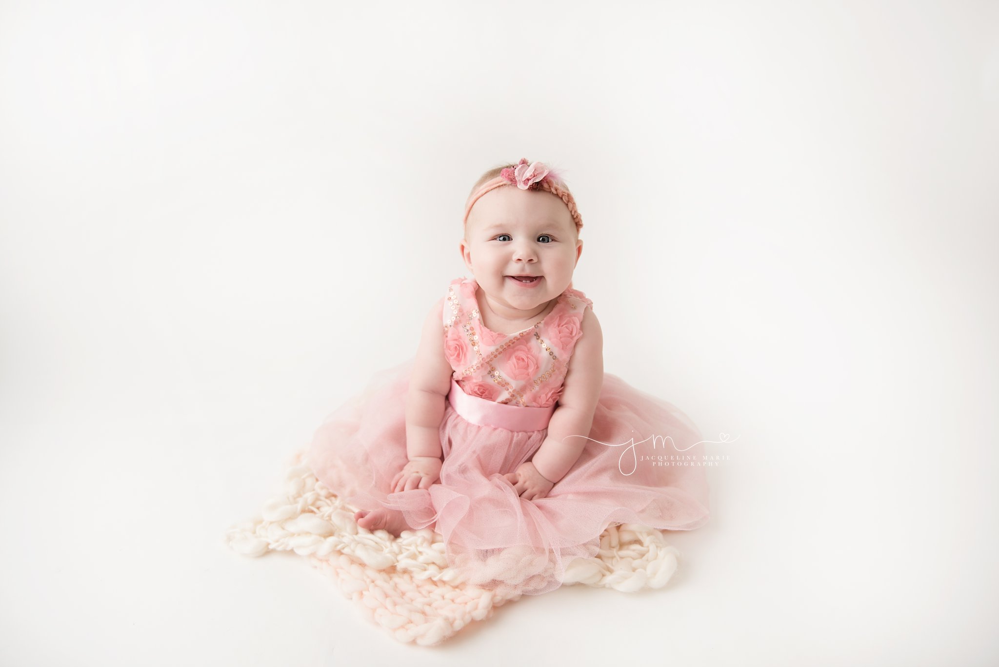 6 month old baby girl wears pink dress her grandmother got her while smiling at jacqueline marie photography studio in columbus ohio