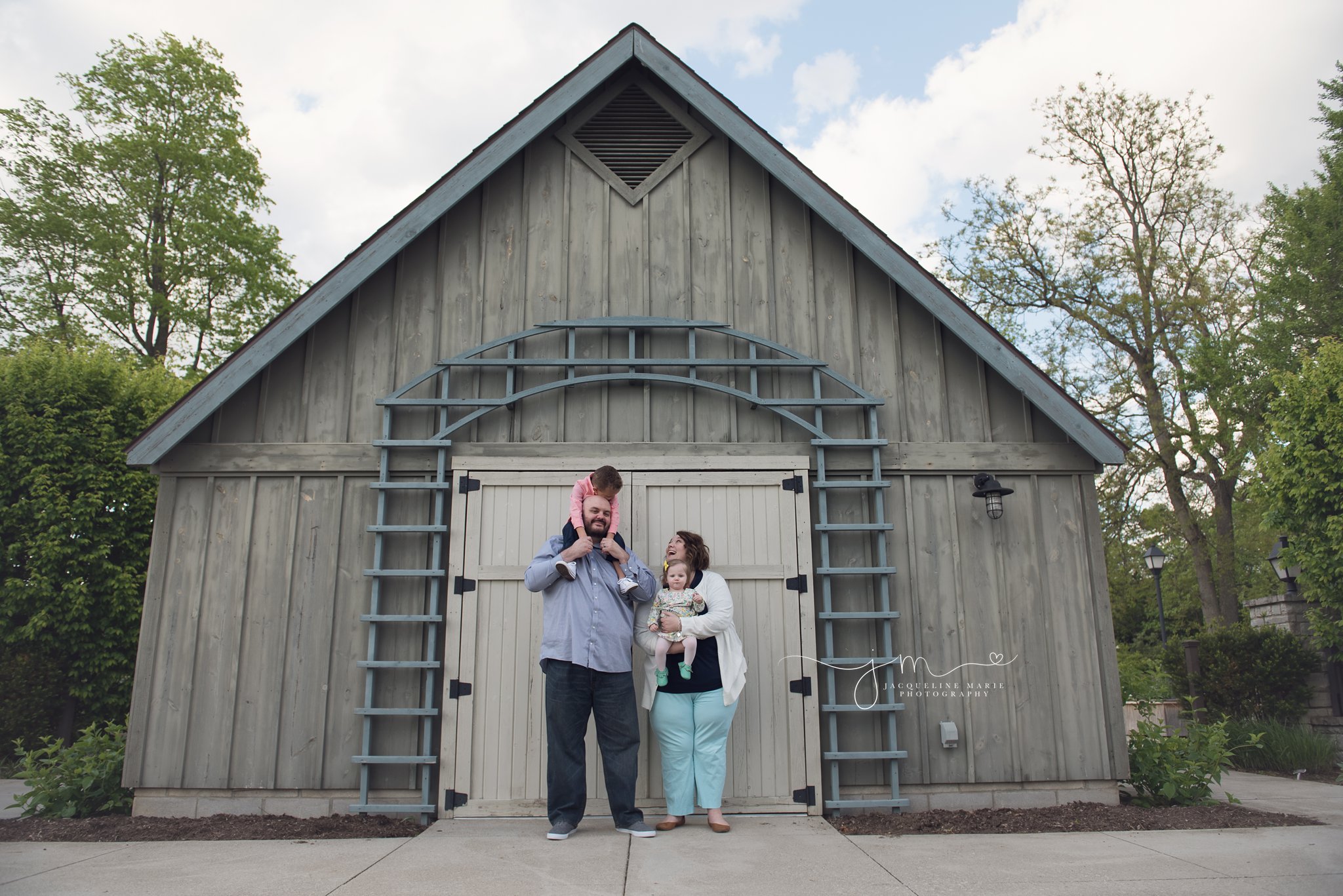columbus ohio family photographer features mother and father holding son and daughter for adoption pictures in front of barn at franklin park conservatory