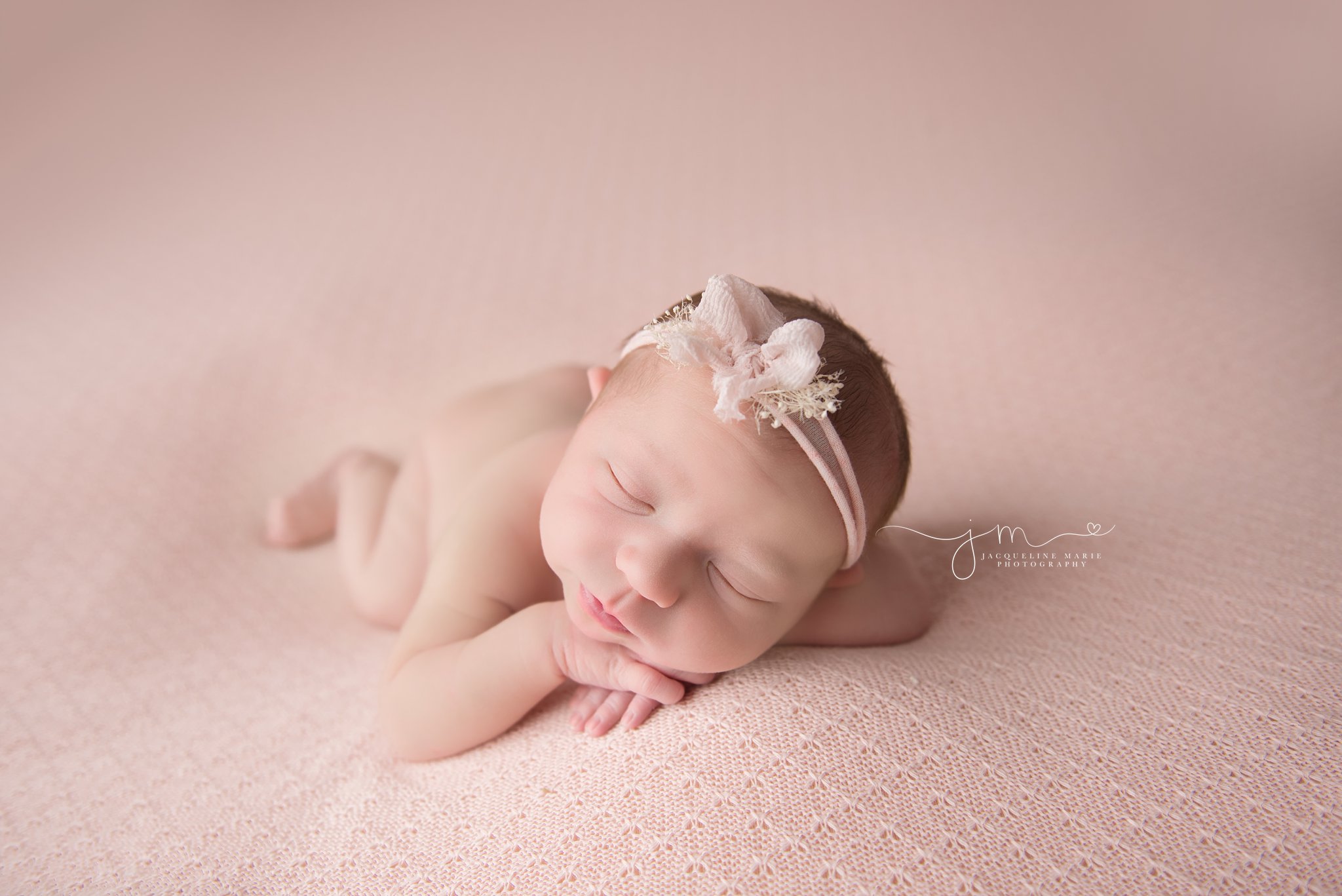 columbus ohio newborn baby girl lays on pink knitted blanket and wears headband with pink bow for newborn photography portraits 