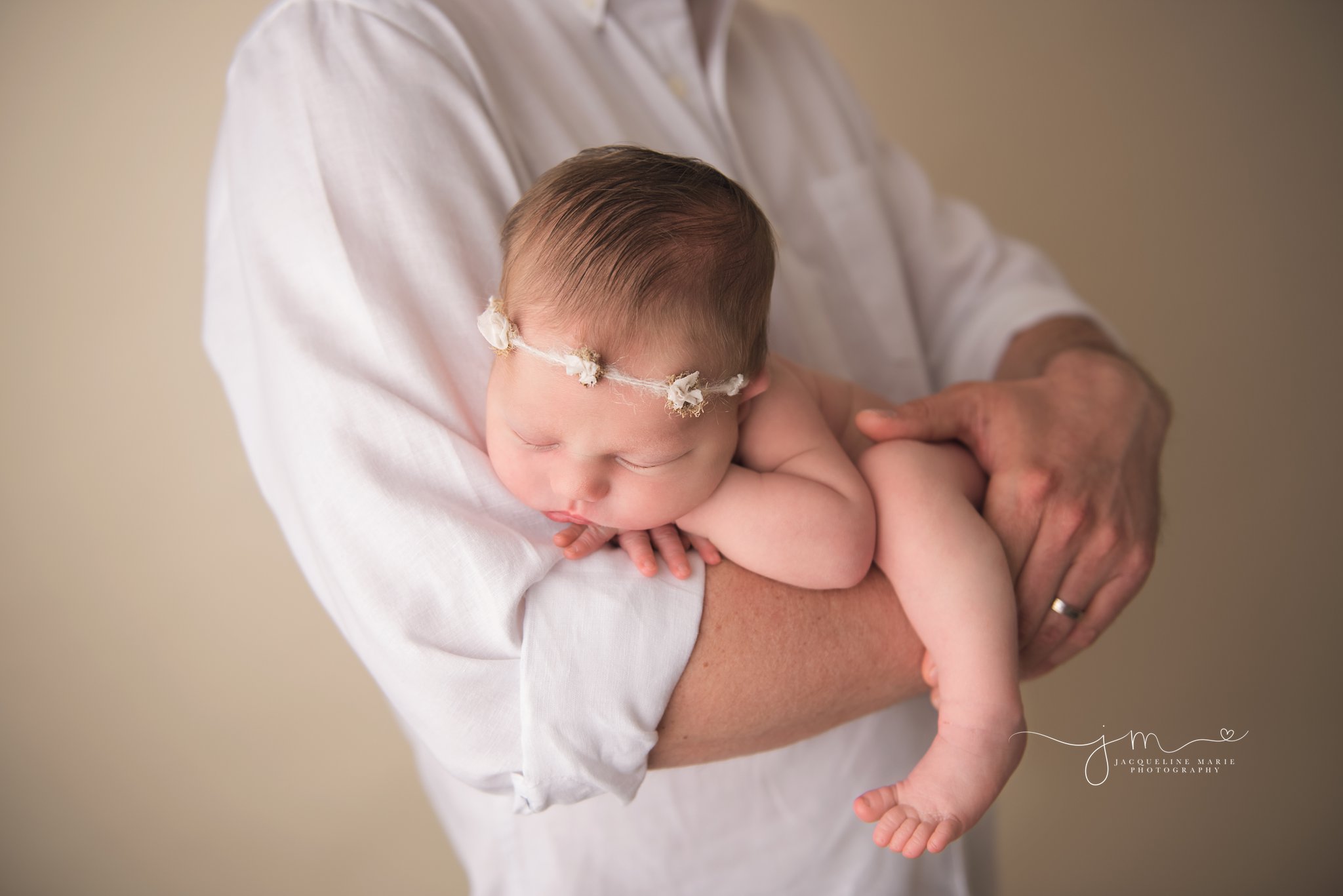 newborn baby girl wears white headband while sleeping in dad'd arms for newborn portraits in columbus ohio