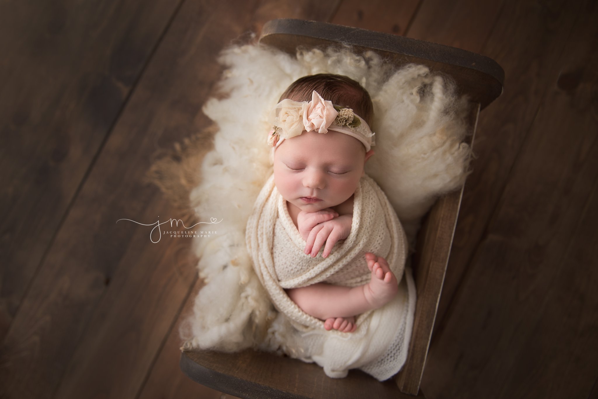 columbus ohio newborn baby girl is swaddled in cream wrap and laying in wood bed for newborn photography portraits at jacqueline marie photography studio