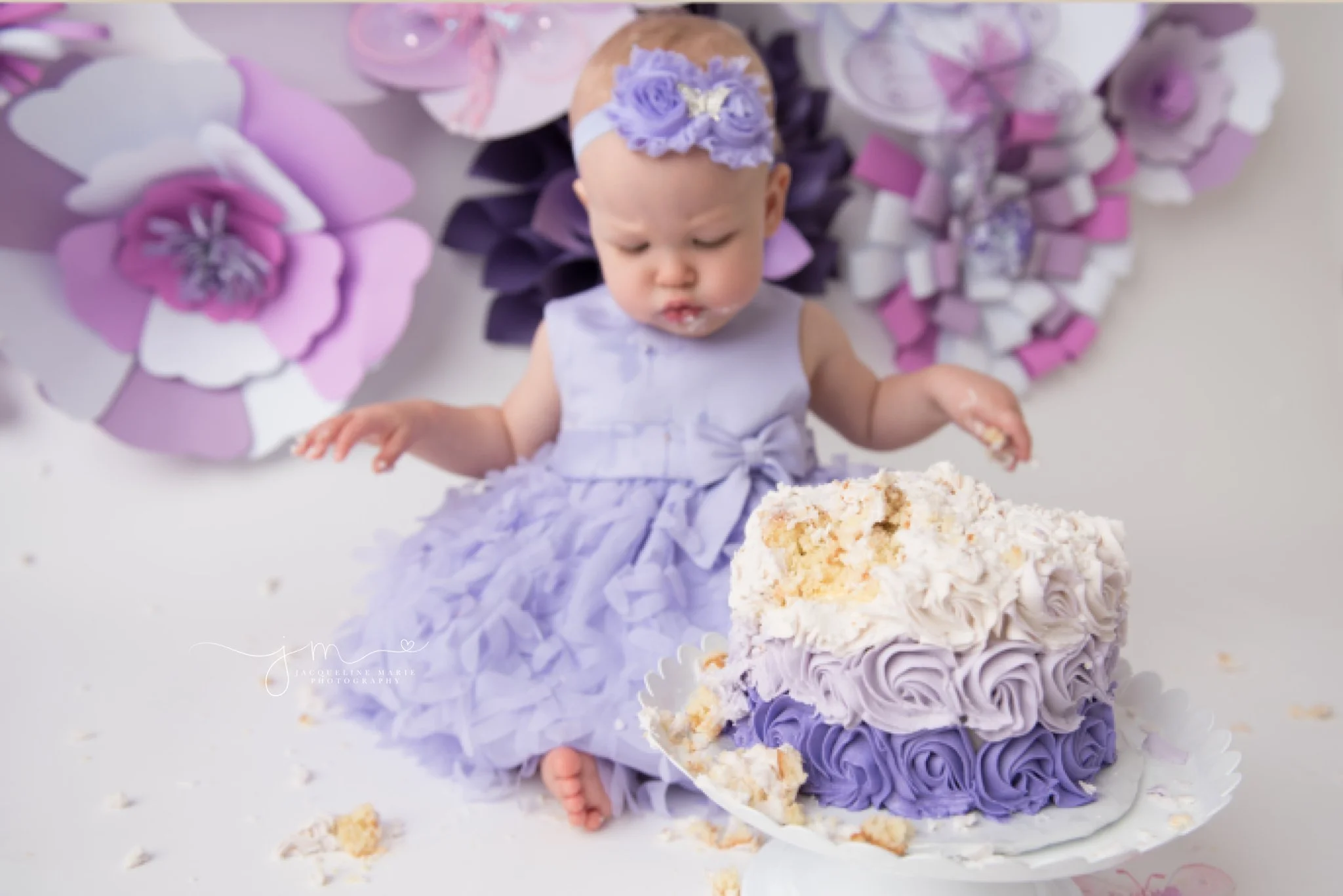 1 year old Adalyn crumbles and eats cake while wearing purple headband and matching dress for her first birthday milestone cake smash pictures in columbus ohio