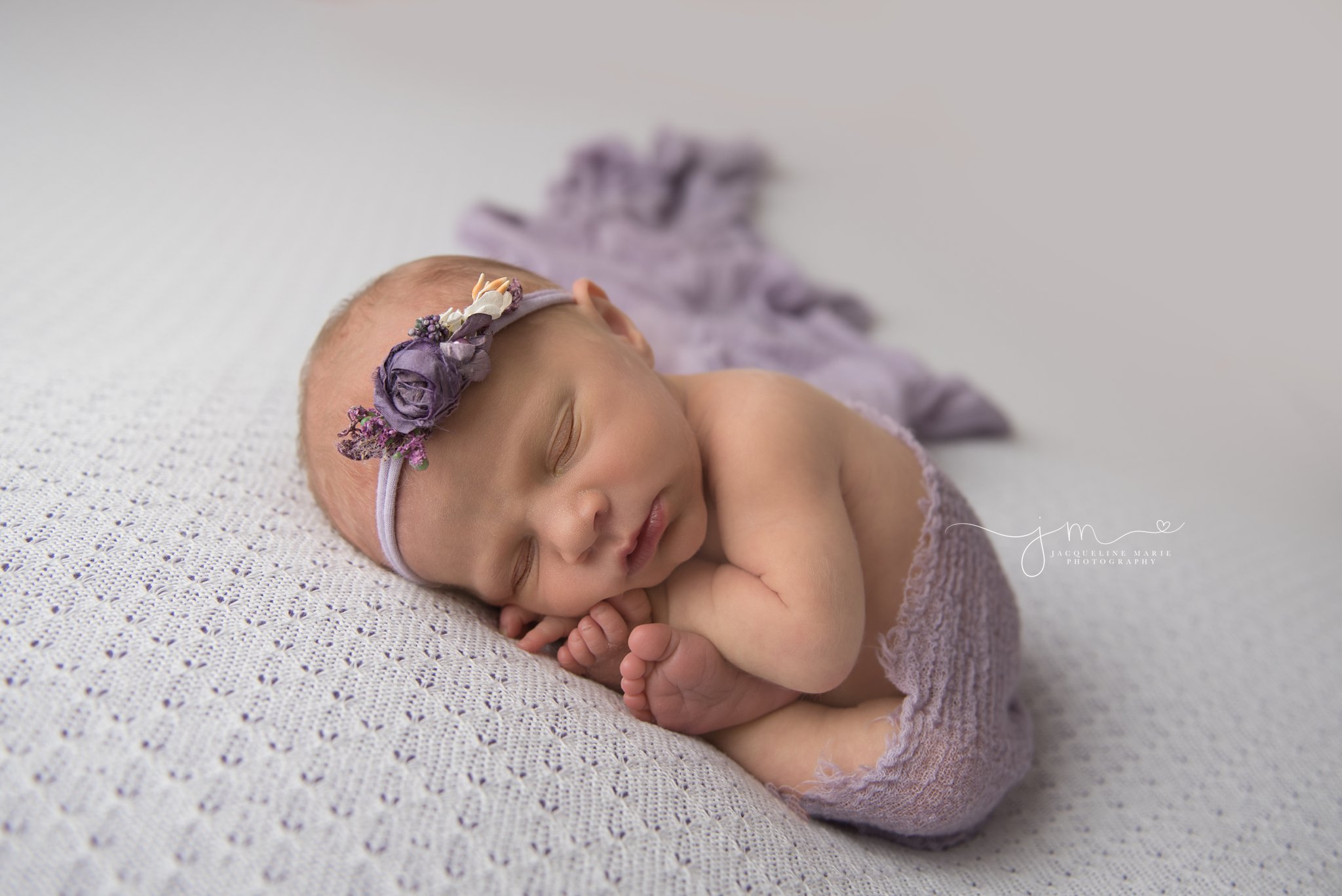 columbus ohio newborn baby girl is wrapped in purple wrap and flower headband for newborn pictures by jacqueline marie photography 