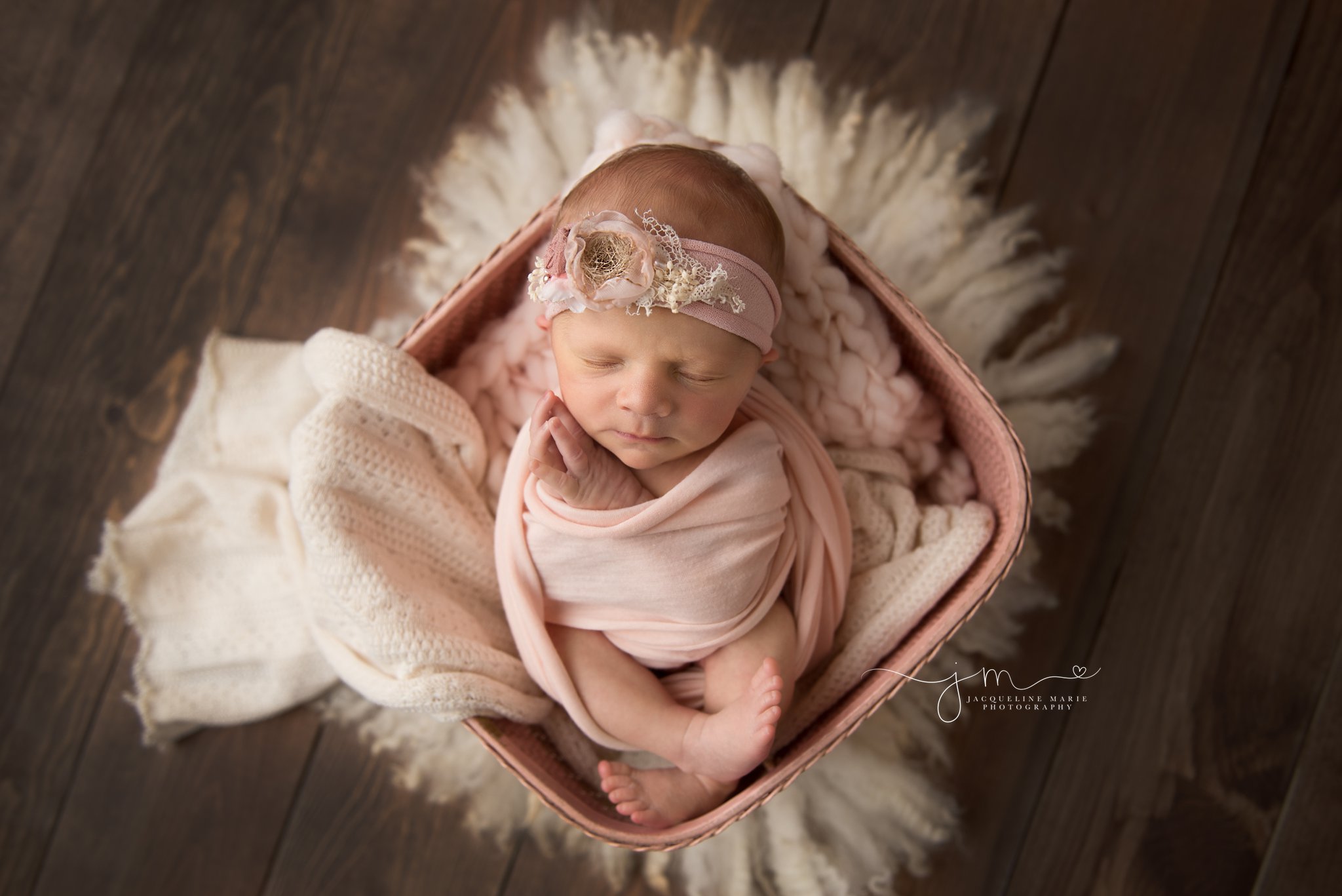 columbus ohio newborn baby girl folds hands near face while swaddled in pink basket for newborn photos 