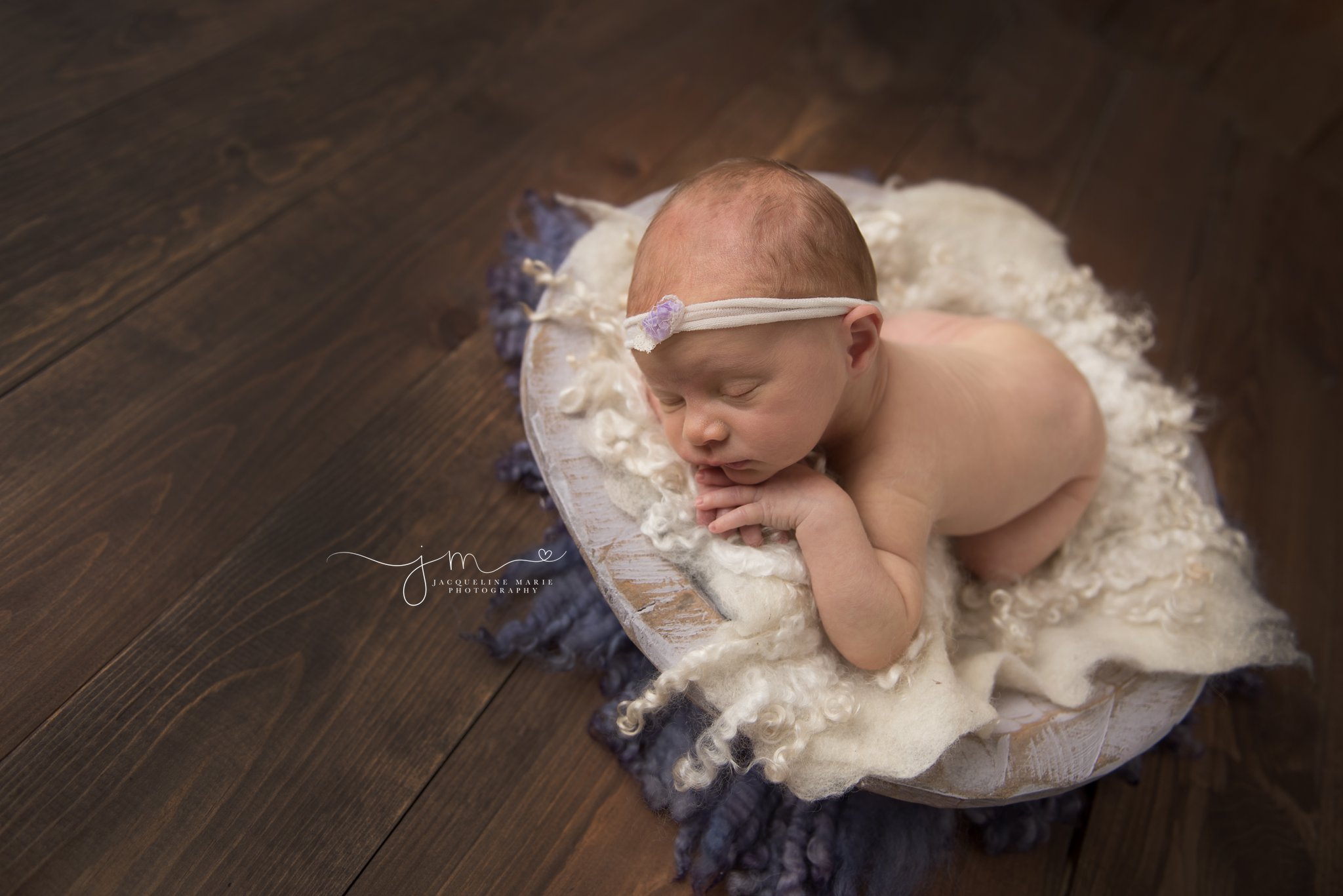 newborn baby girl is posed in a lavender purple bowl on wood flooring in columbus ohio for newborn photography session at jacqueline marie photography studio