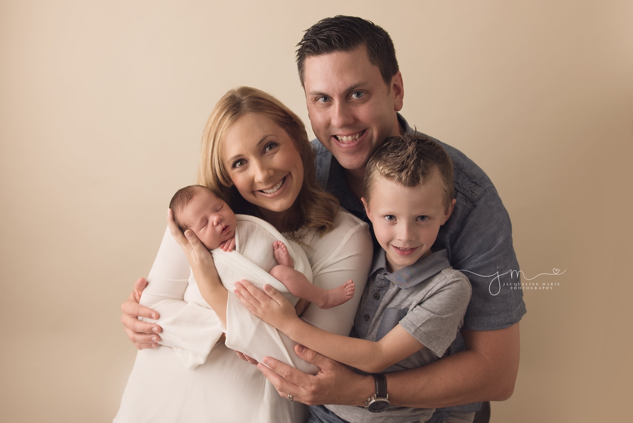 columbus ohio family of four welcomes newborn baby boy and holds him while smiling at jacqueline marie photography studio