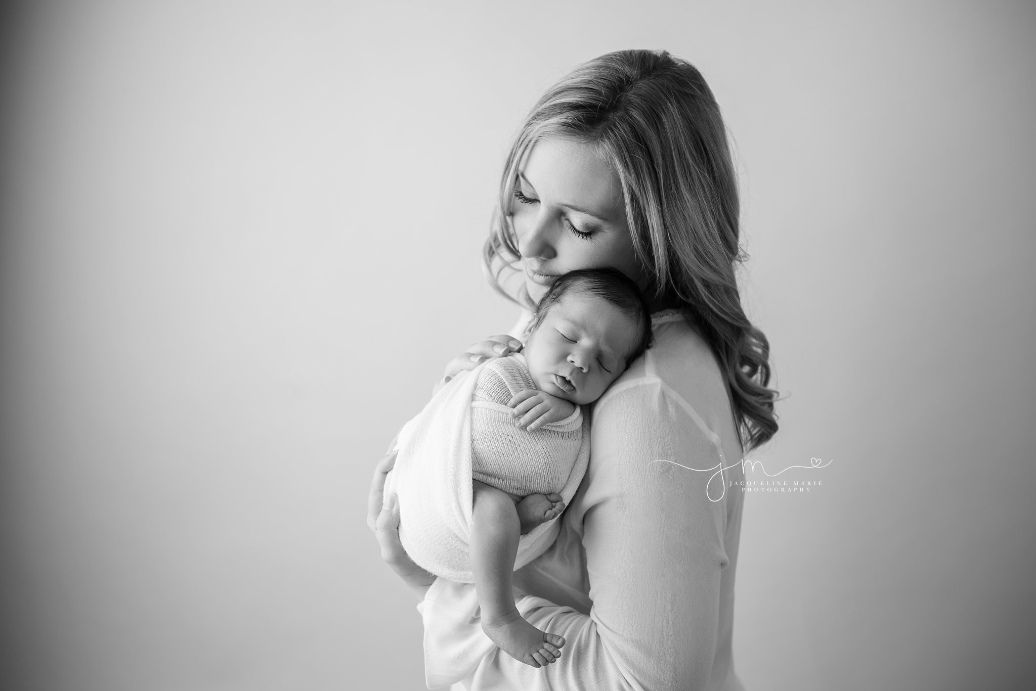 mother holds newborn baby boy and touches his back for newborn pictures in columbus ohio