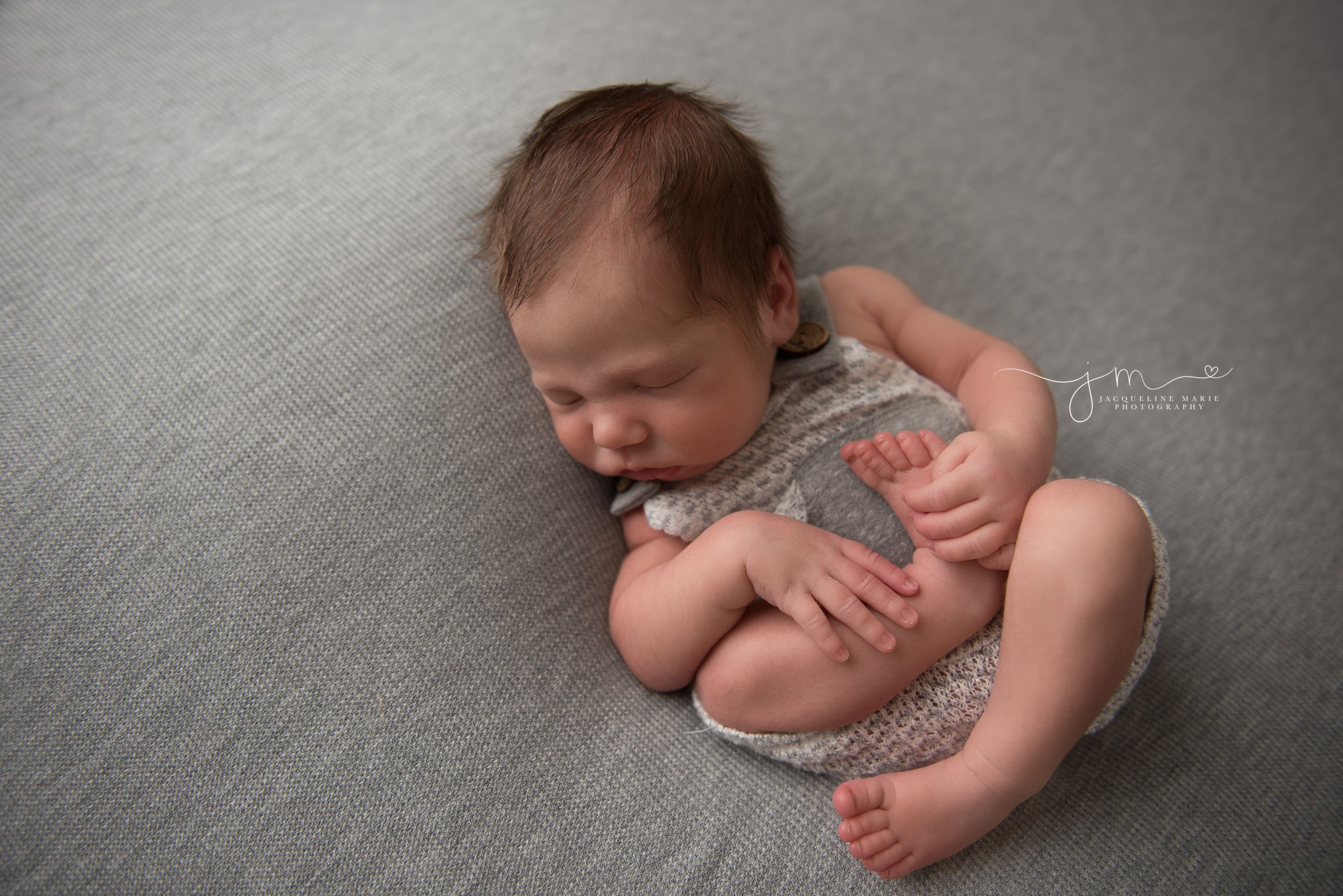 columbus ohio newborn baby wears gray and white romper while holding feet at jacqueline marie photography newborn studio