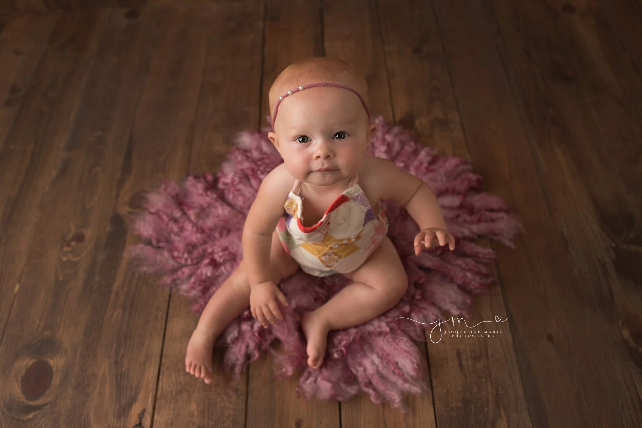 8 month old Scarlett sits on pink felted layer and wood floor for baby milestone pictures in columbus ohio