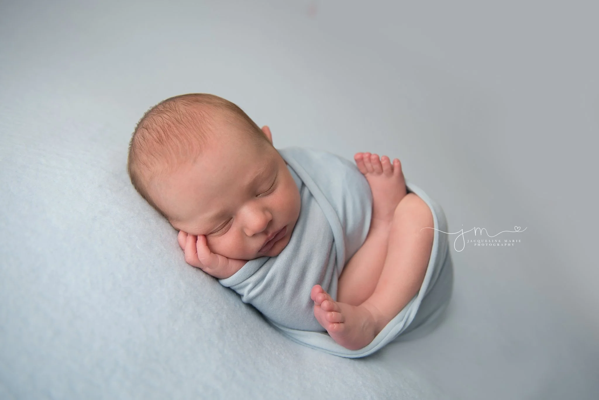 1 week old newborn baby boy is wrapped in blue with hand on his face in columbus ohio