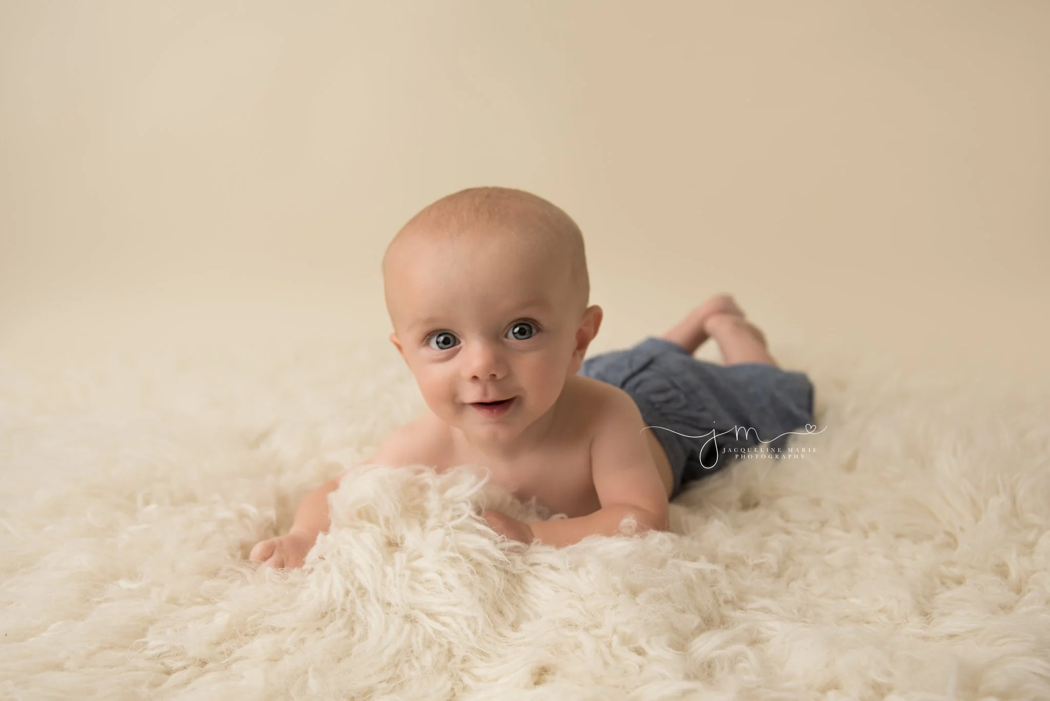 6 month old Caiden has bright blue eyes and smiles on cream rug in columbus ohio for baby photography session 