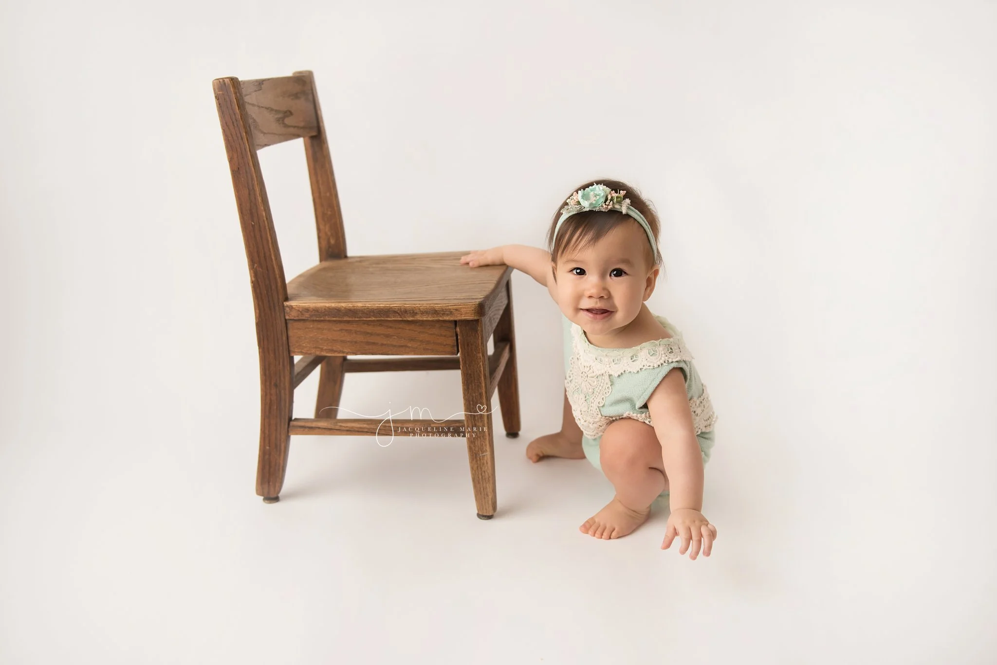 baby girl wears mint and cream romper and stands next to wood chair for first birthday milestone pictures in columbus ohio