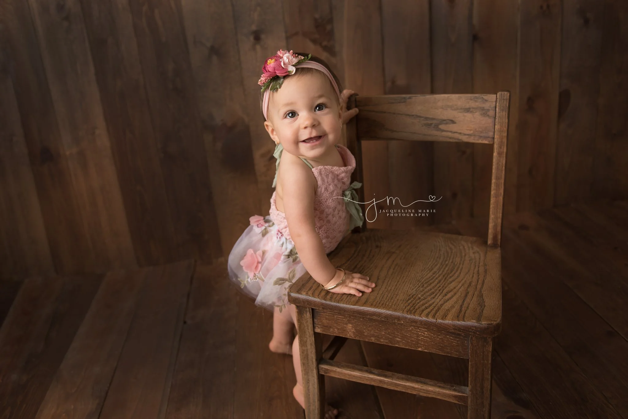 columbus ohio child and baby photographer features image of 1 year old standing at wooden chair while wearing pink and floral romper