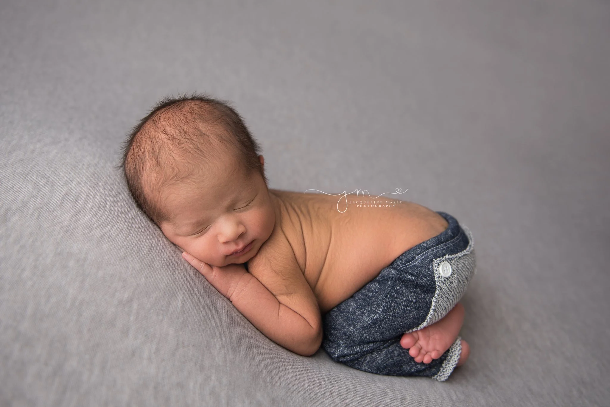 newborn baby boy wears navy blue pants while posed on gray blanket in columbus ohio newborn photography studio