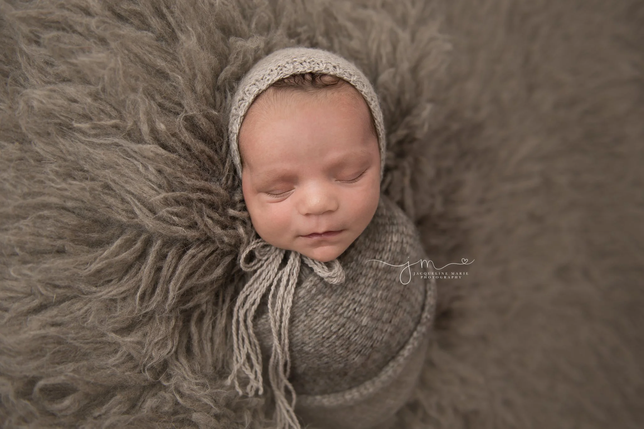 newborn baby boy is swaddled in gray wrap and bonnet on matching float rug in columbus ohio newborn photography studio
