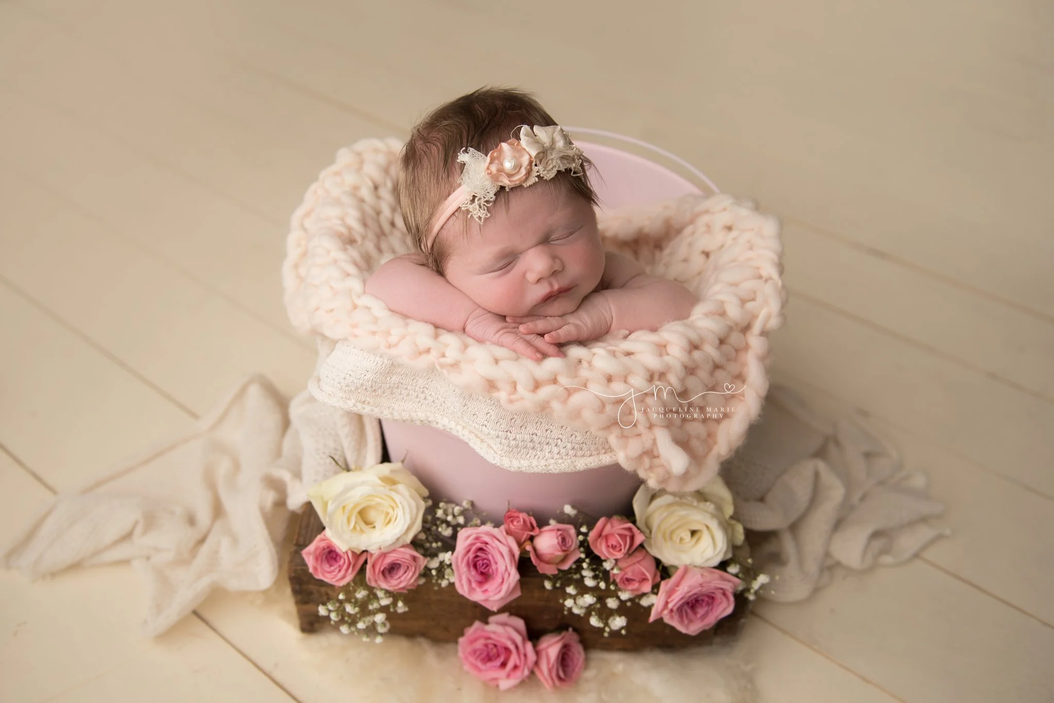 1 week old newborn baby girl is sleeping in pink bucket surrounded with pink and cream roses in columbus ohio newborn photography studio