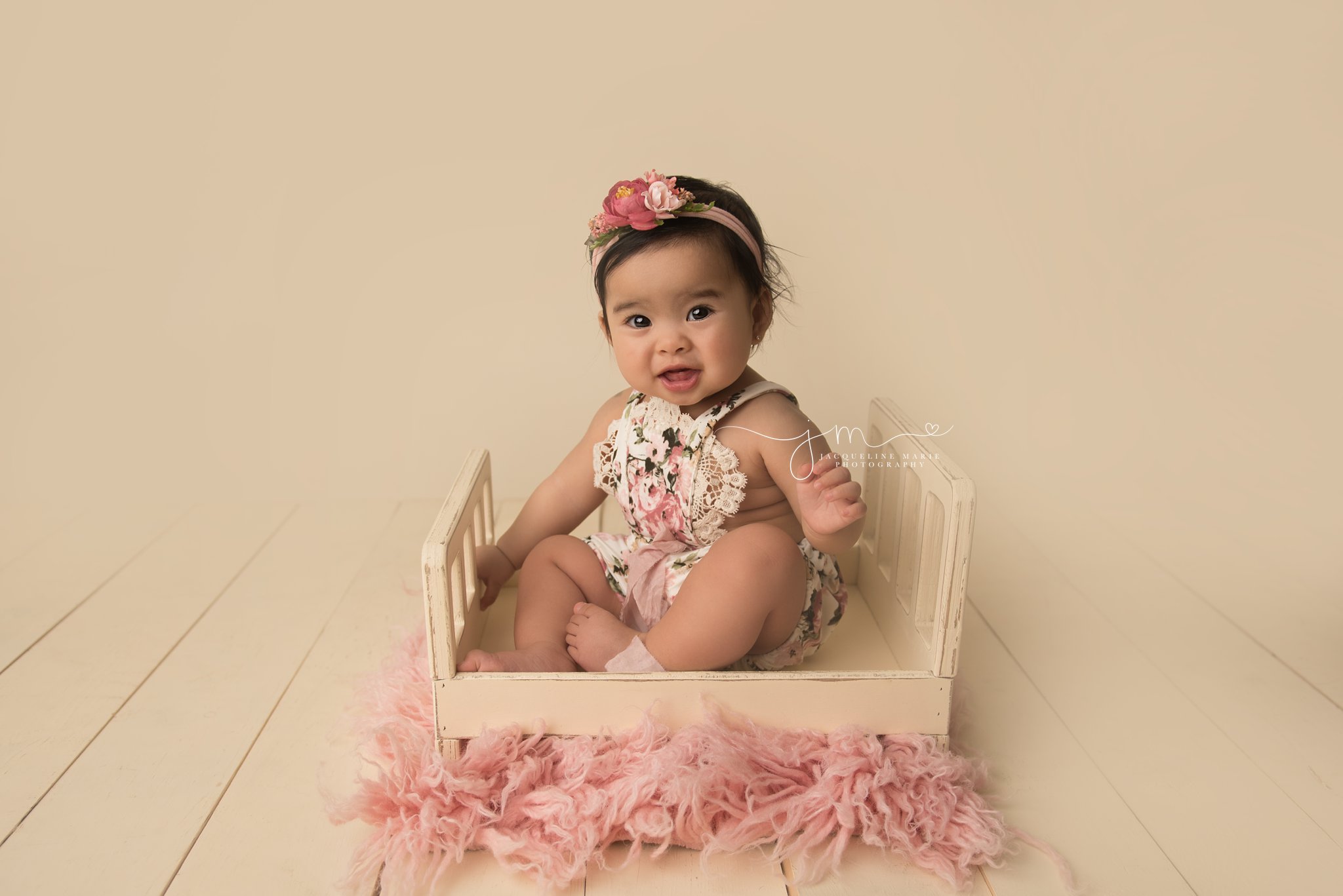 1 year old baby girl wears floral romper while sitting in cream wood bed prop in columbus ohio for first birthday portraits