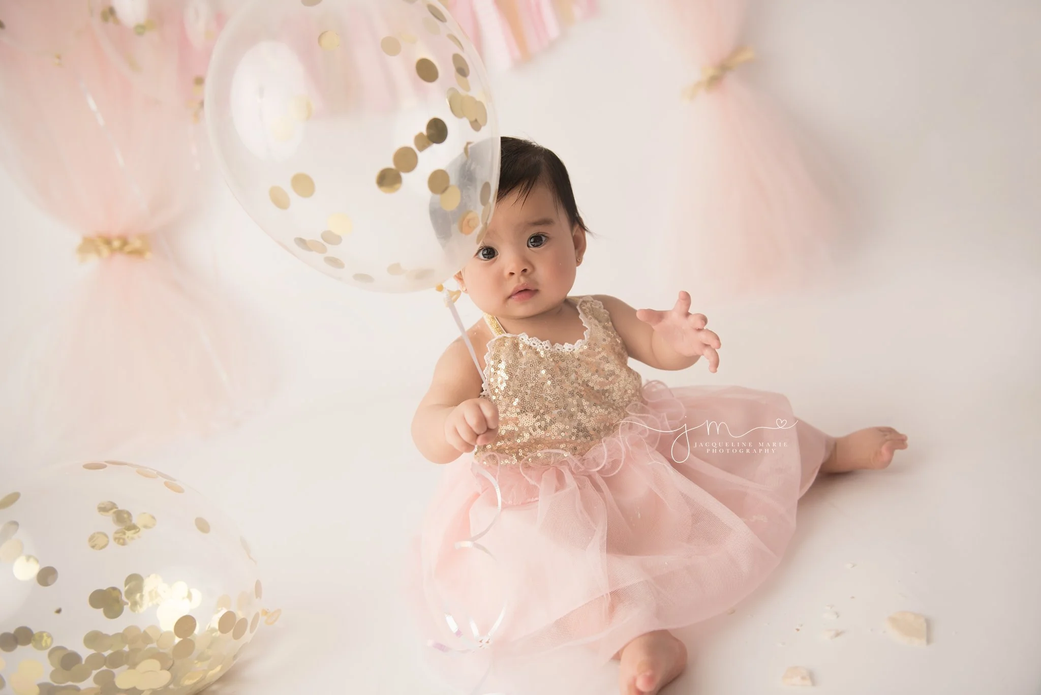 1 year old holds gold confetti balloon for first birthday cake smash session in columbus ohio