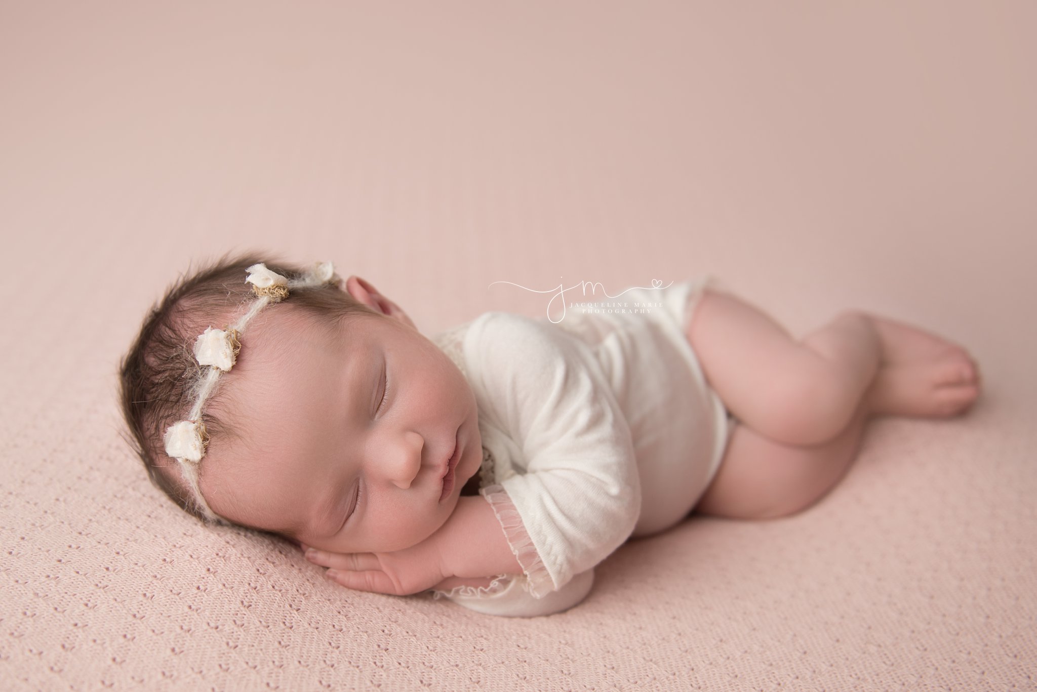 1 week old newborn baby girl wears cream headband and romper while sleeping for newborn photography session