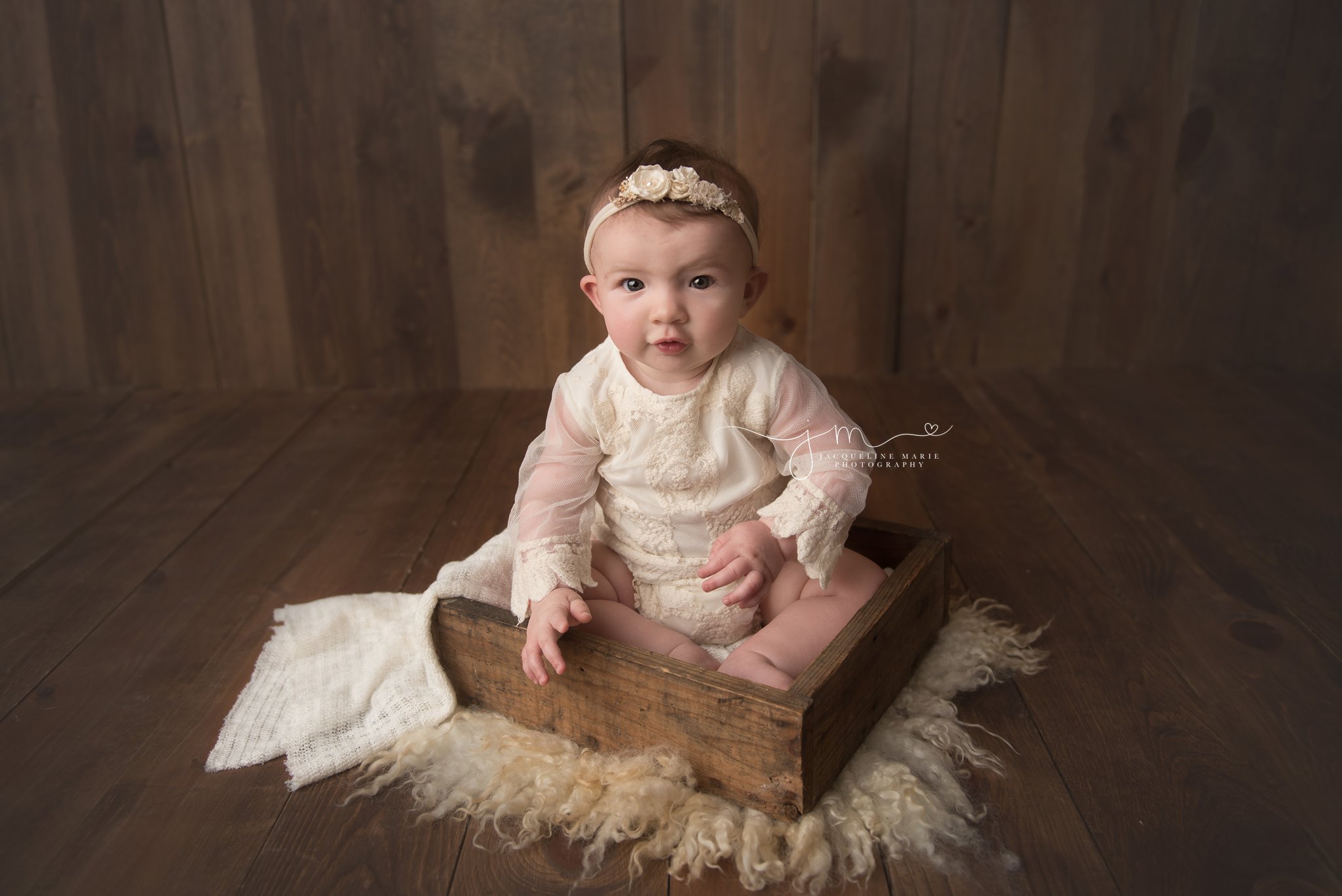 columbus ohio baby girl wears cream lace romper while sitting in wood prop box for milestone pictures