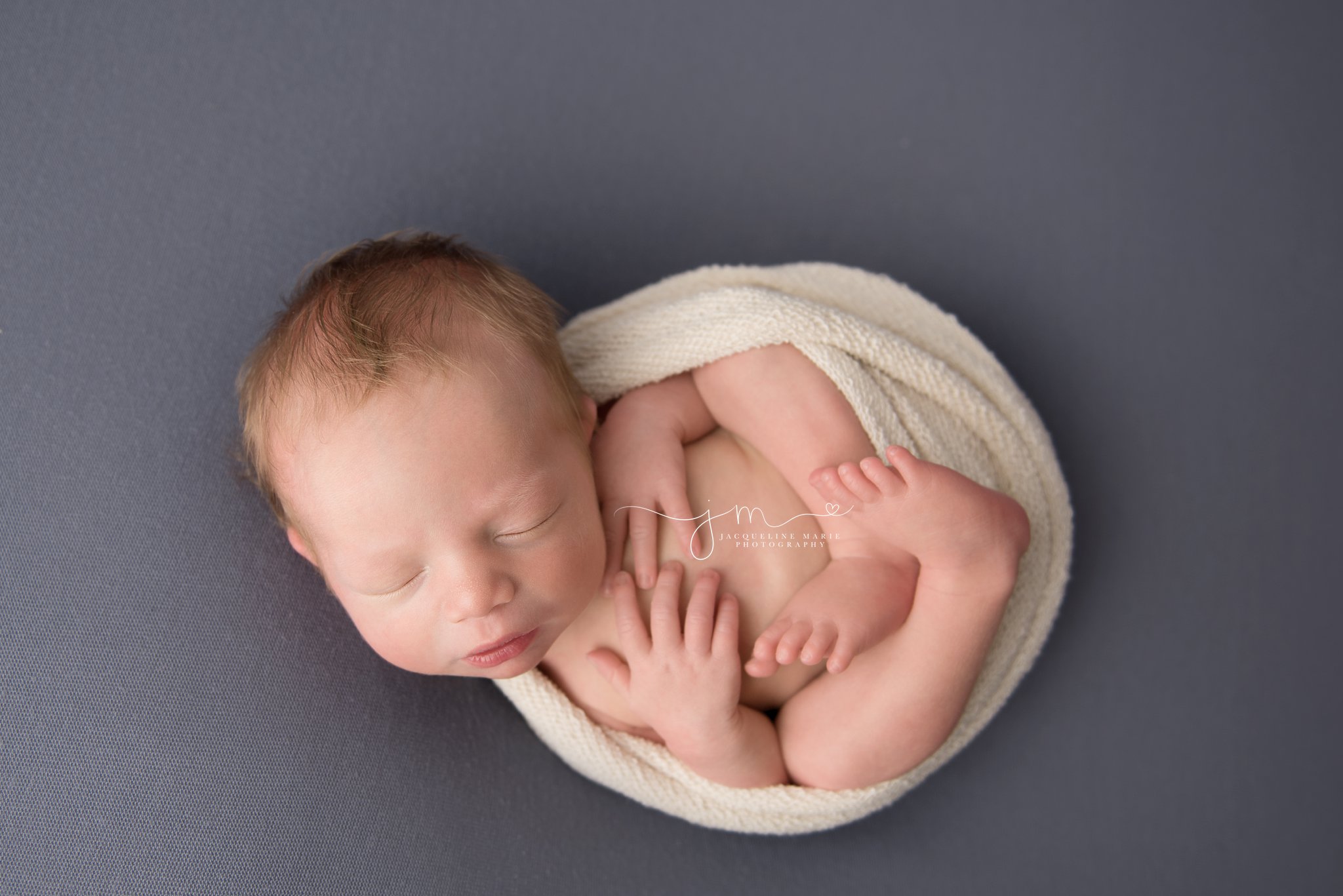 newborn baby is wrapped in cream wrap with hands on chest for newborn photography session in columbus ohio