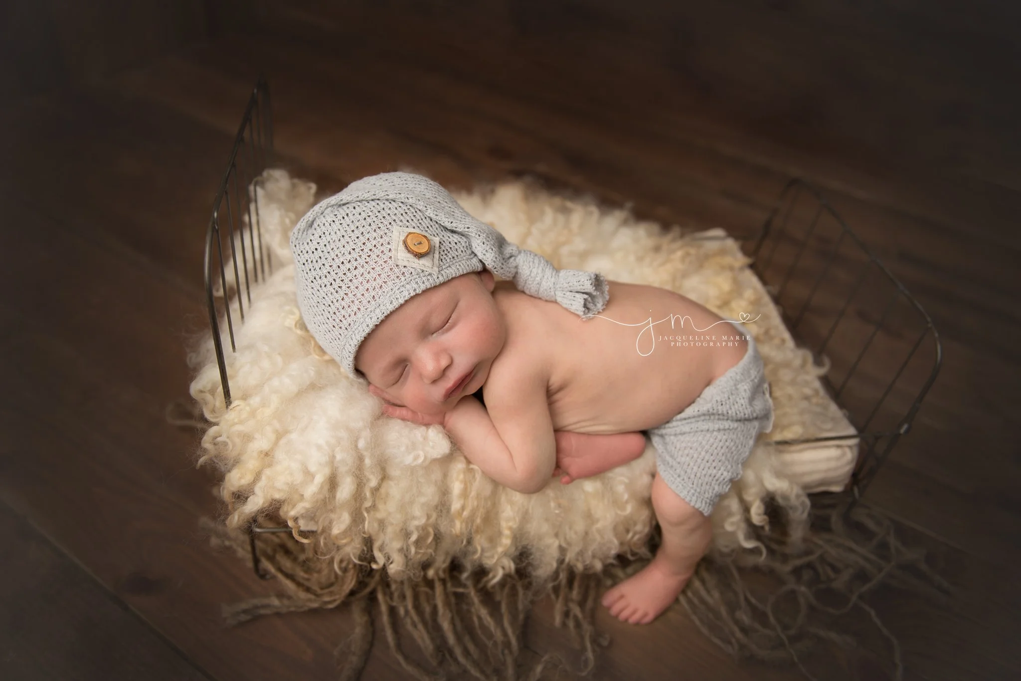 newborn baby boy wears hat and shorts while posed on baby bed in columbus ohio photography studio