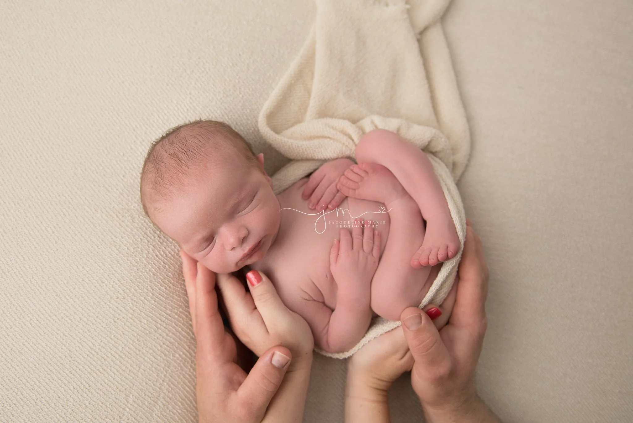 newborn baby boy is wrapped in cream wrap with his parent’s hands holding him during newborn photography session in columbus ohio