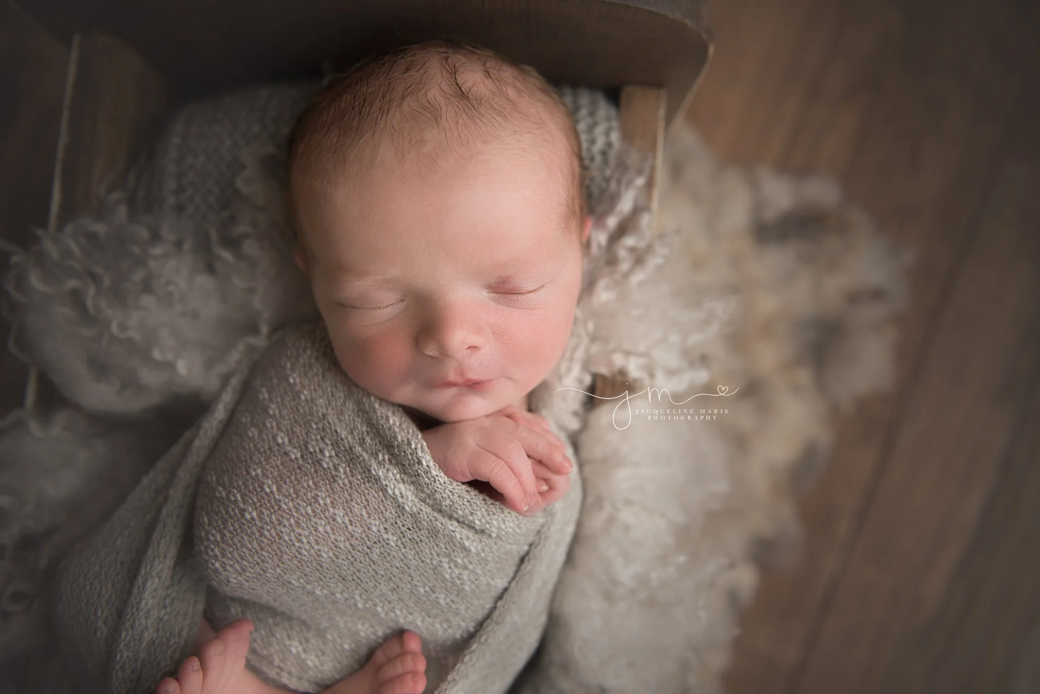 1 week old newborn baby boy is swaddled in gray wrap while sleeping in wood bed during newborn pictures in columbus ohio studio