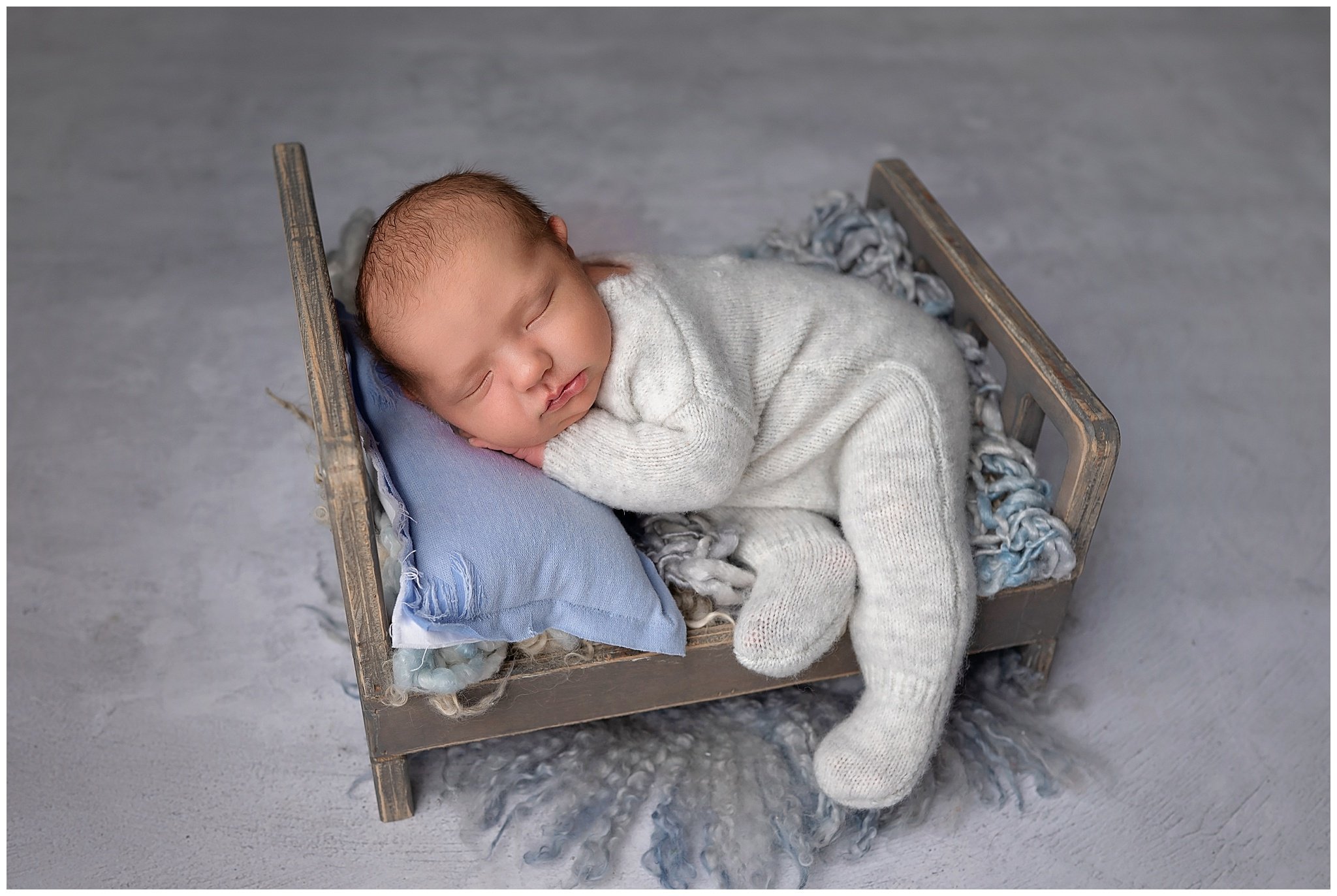 newborn baby boy wears gray sleeper posed on a baby bed in Columbus Ohio