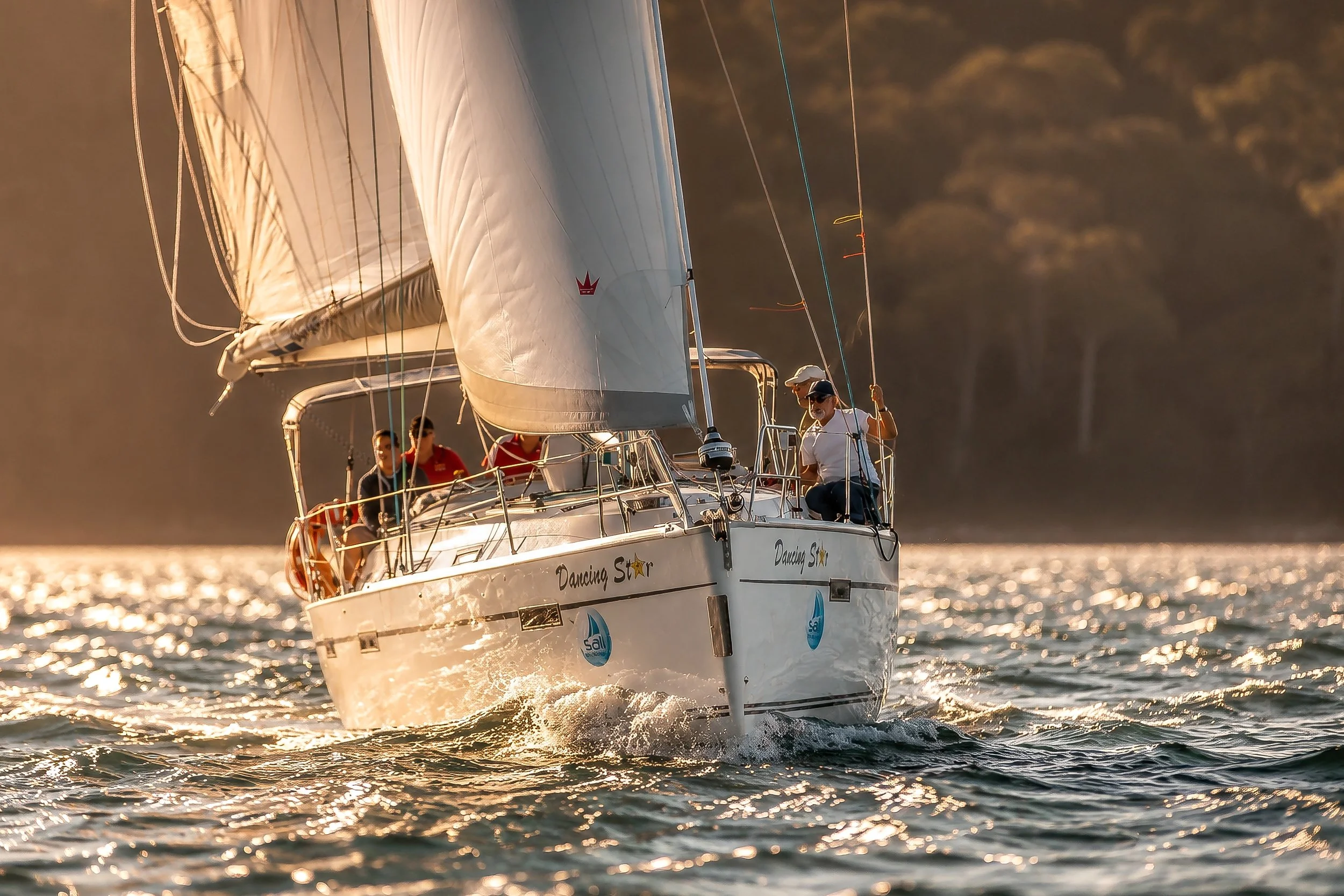 A sailboat named 'Dancing Star' sailing on water during sunset with four people on board, surrounded by shimmering waves.