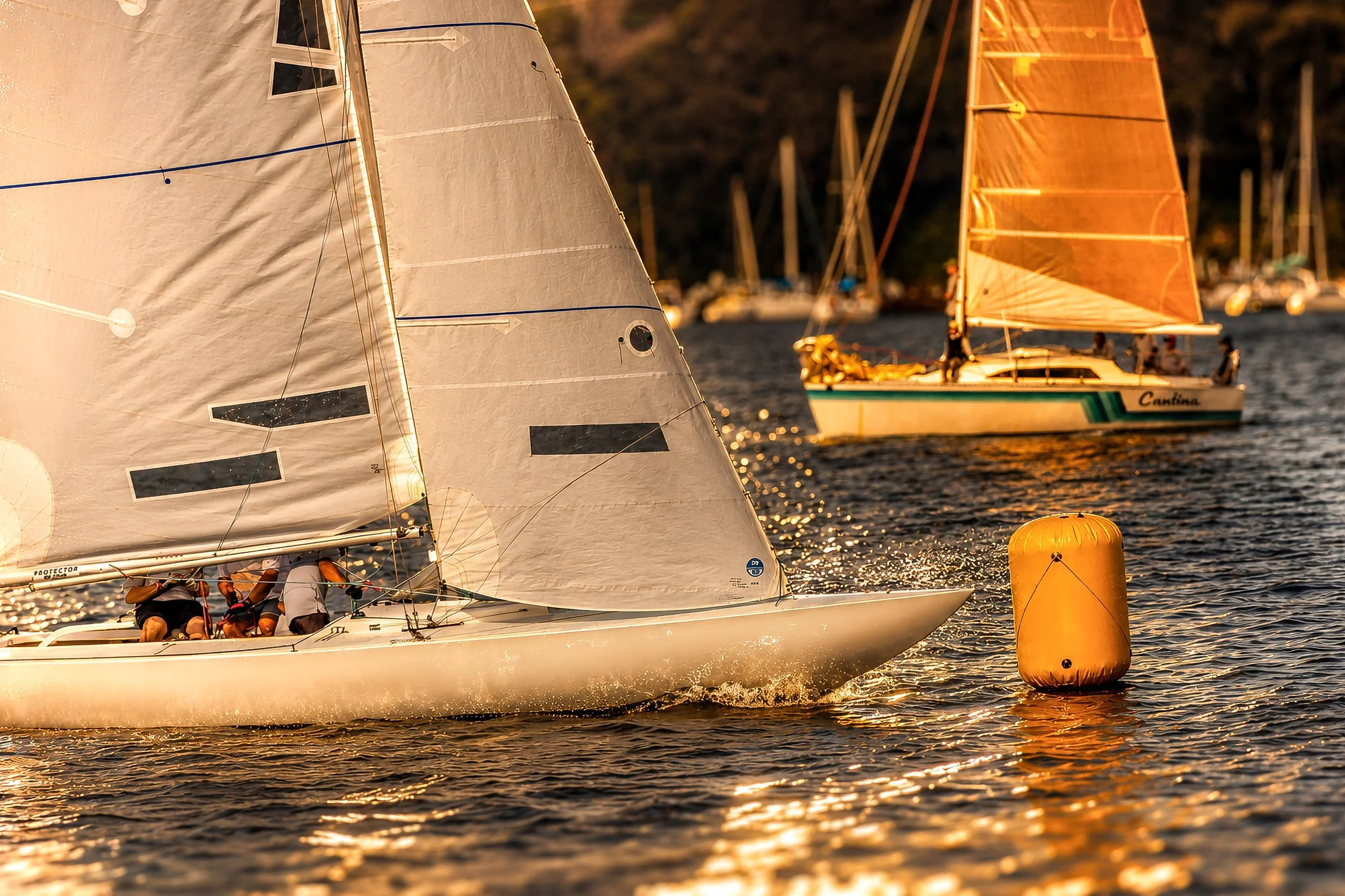 Sailboats racing on the water near a yellow buoy with a sunset backdrop.