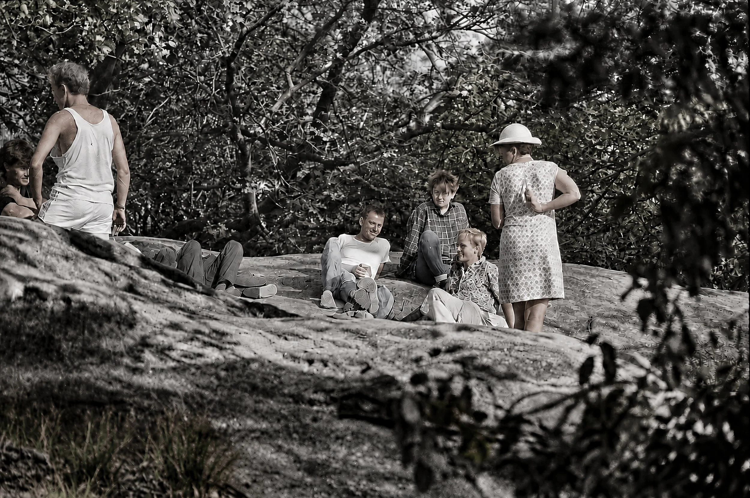 Summer by the River - A group of people relaxes among the rocks and trees beside the water. The informal gathering provides a quieter counterpoint to the stockyards and mountain landscapes, capturing a moment of leisure during the journey through cou