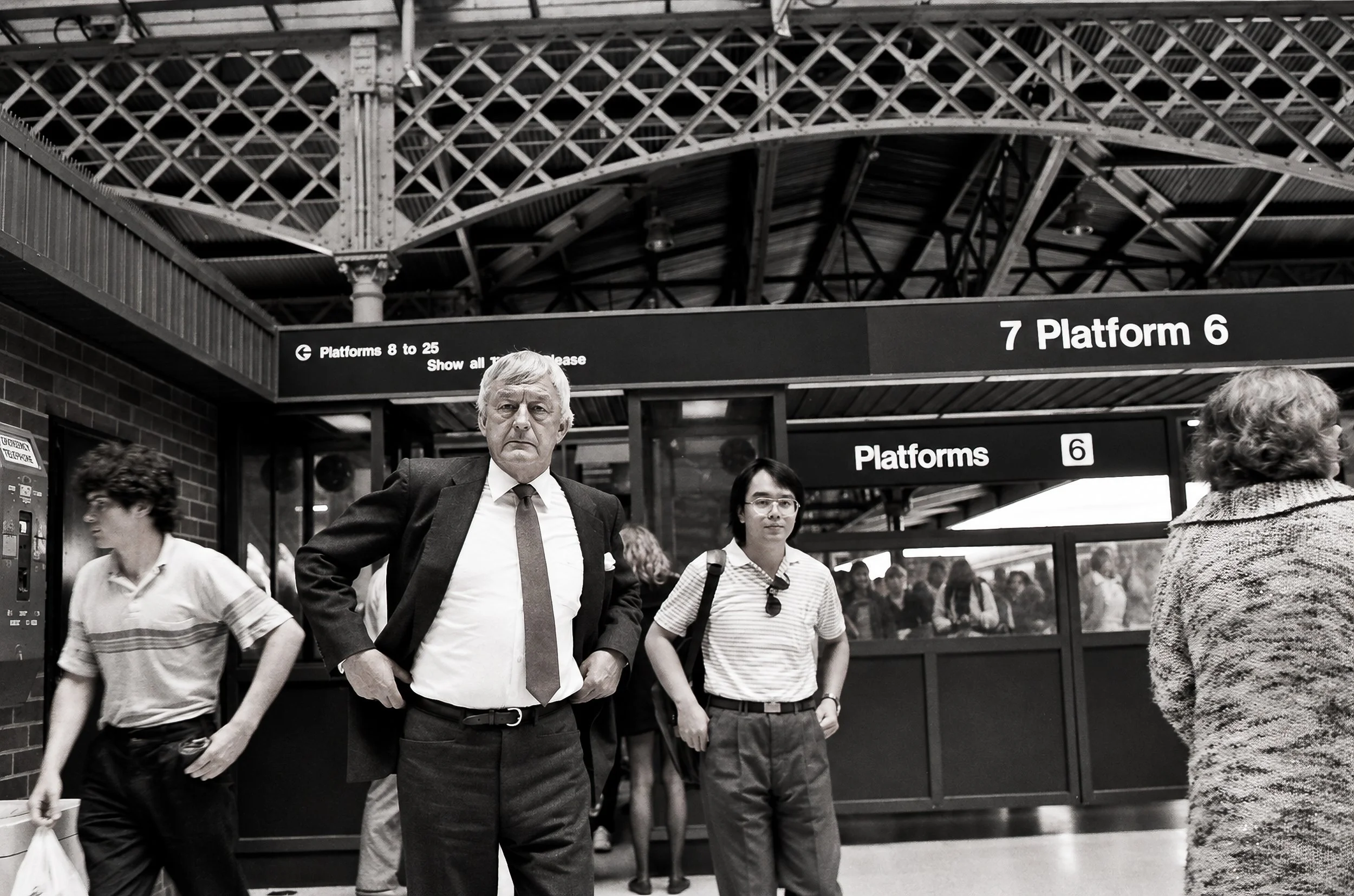 Platform 6 - Passengers emerge beneath the distinctive ironwork of a Sydney railway station. The mixture of business attire, casual clothing, station signage and passing commuters captures an ordinary moment in the city's daily movement.