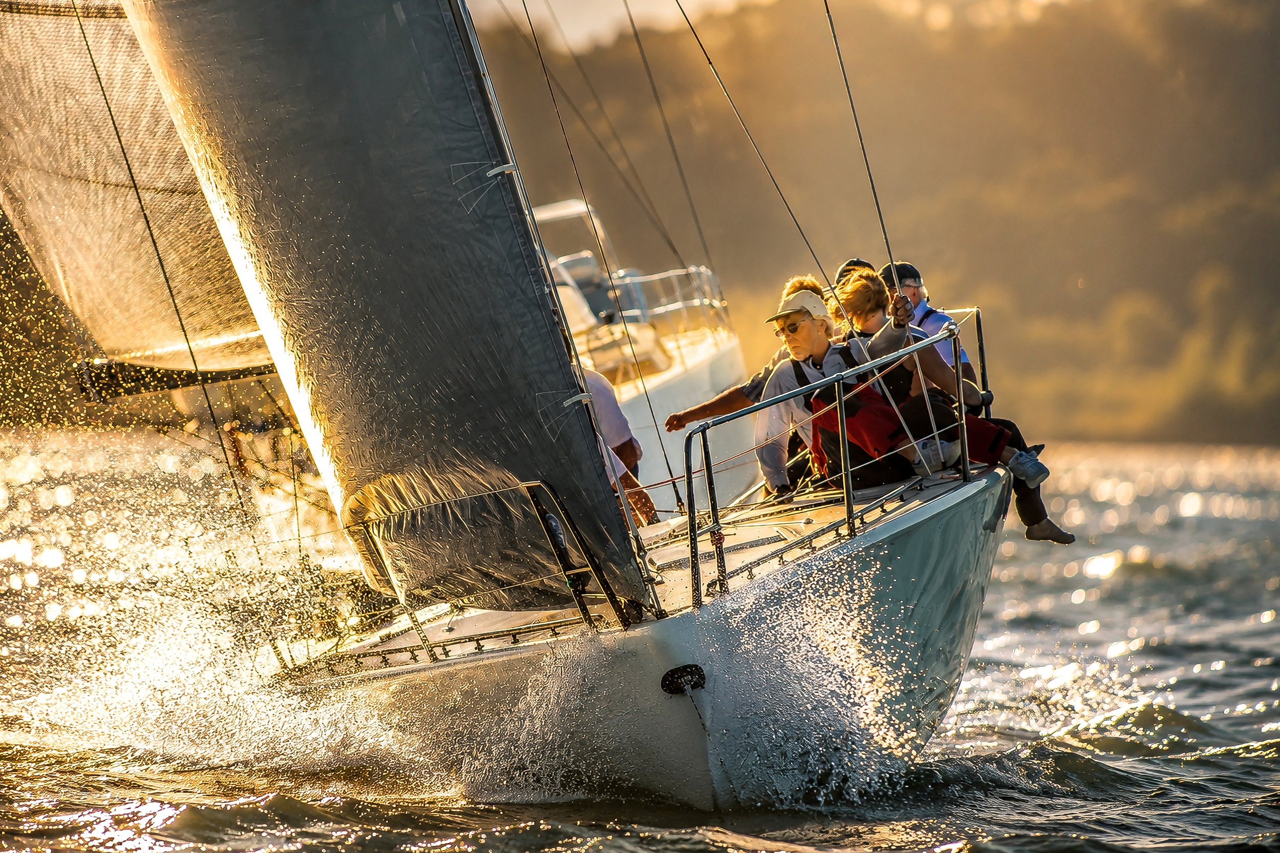 Sailboat with crew members sailing on water during sunset.