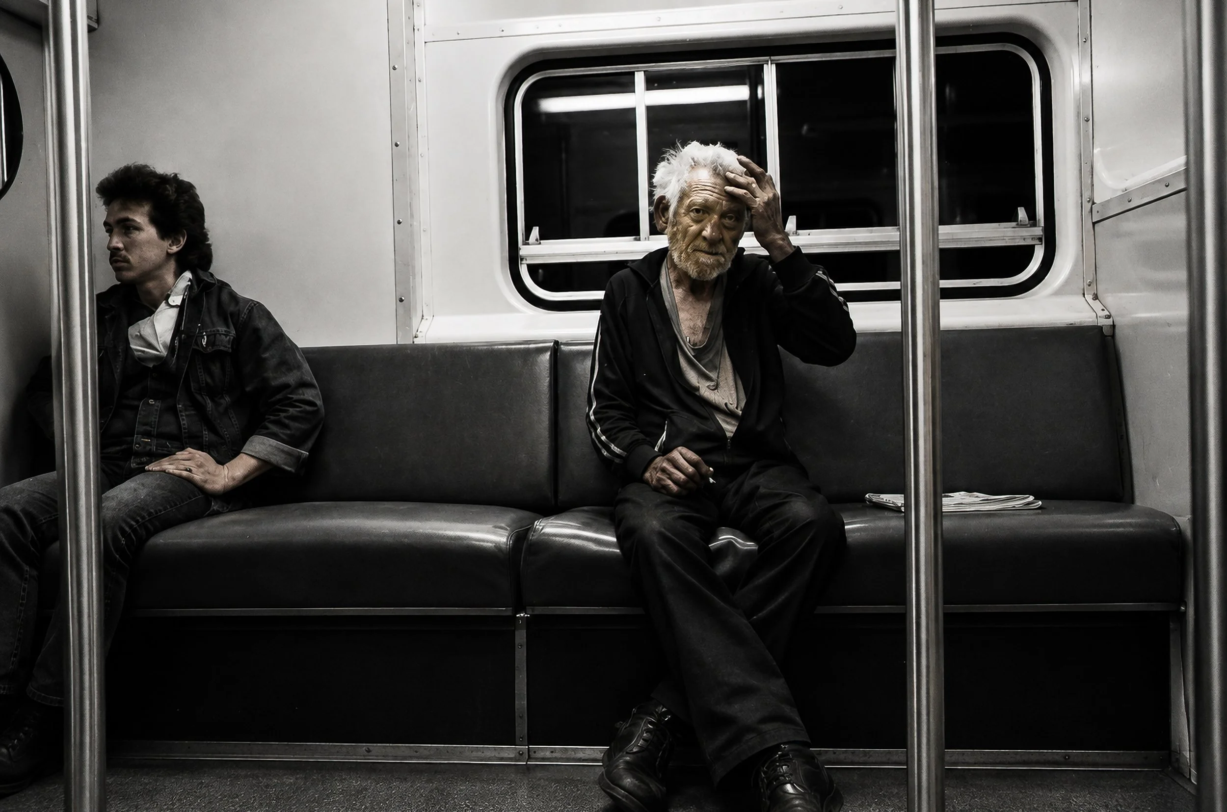 Travellers - Two passengers sit apart inside the carriage, framed by the vertical poles and dark vinyl seating. The contrast between the brightly lit window and the darker clothing creates a quiet, introspective moment.