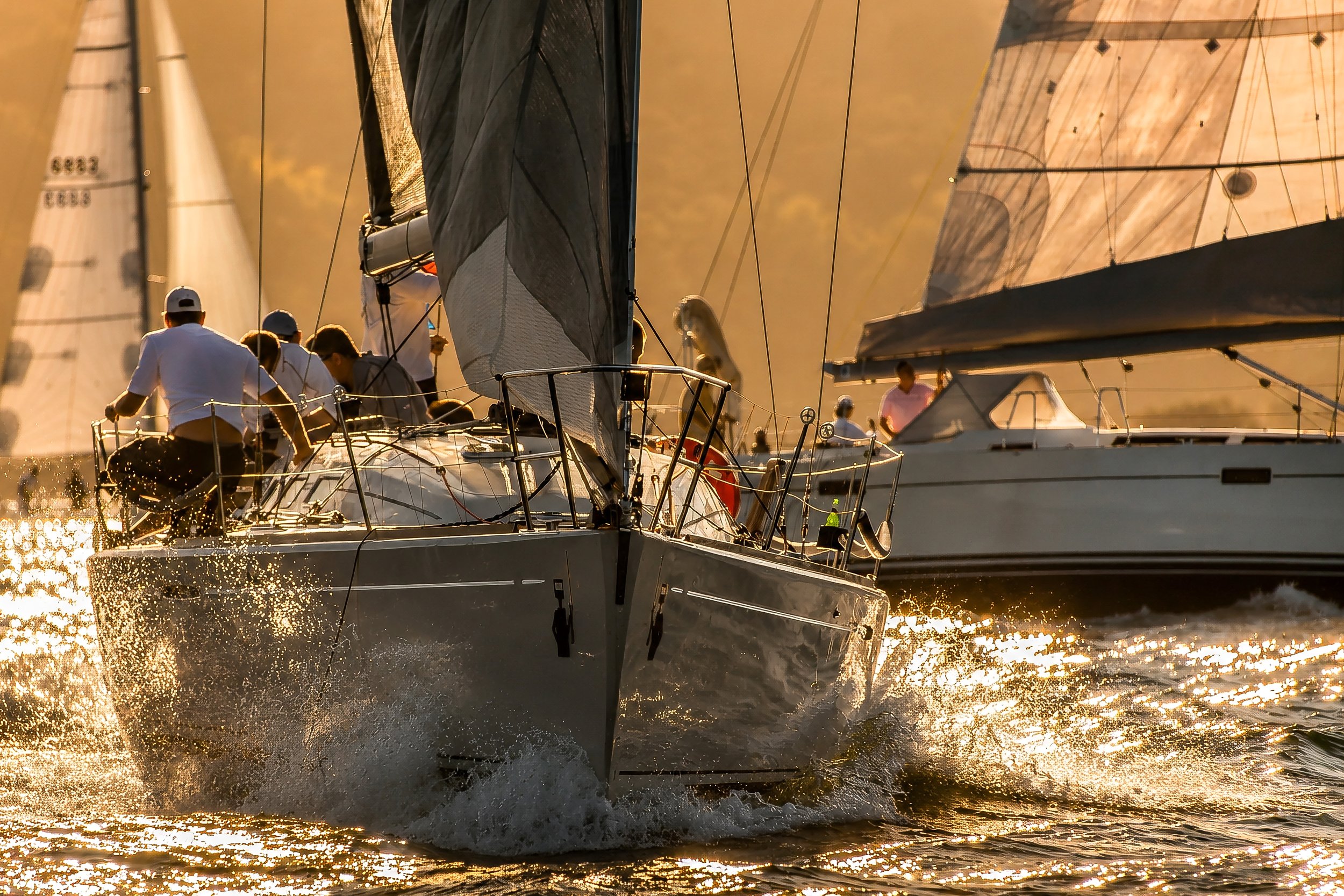 Sailboats sailing on the water at sunset with crew members on deck.