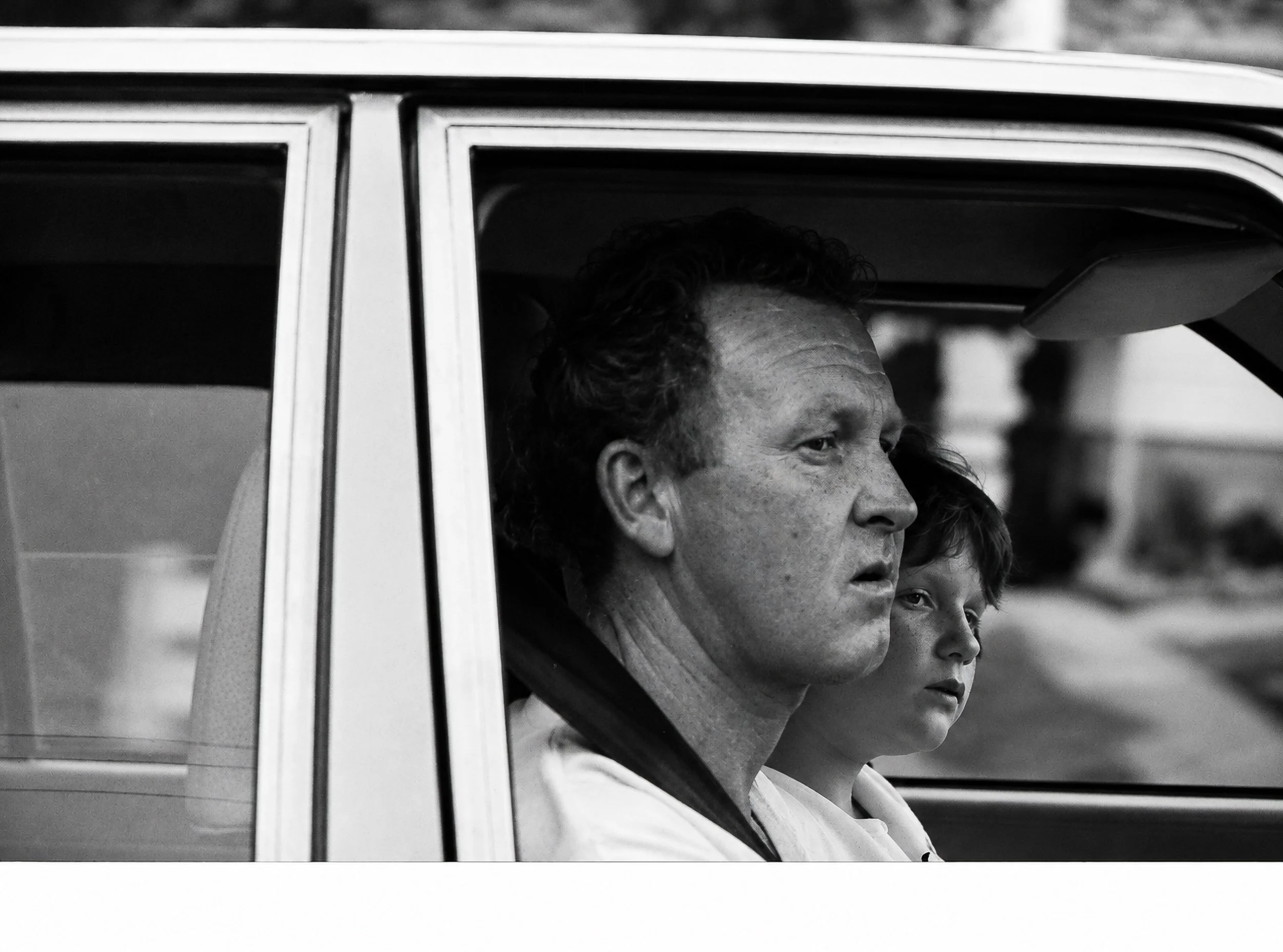 Driver and Passenger - A driver and a passenger are caught together through the side window, both absorbed in the passing moment. Their overlapping faces create a particularly intimate glimpse into the private world of a car moving through the city.