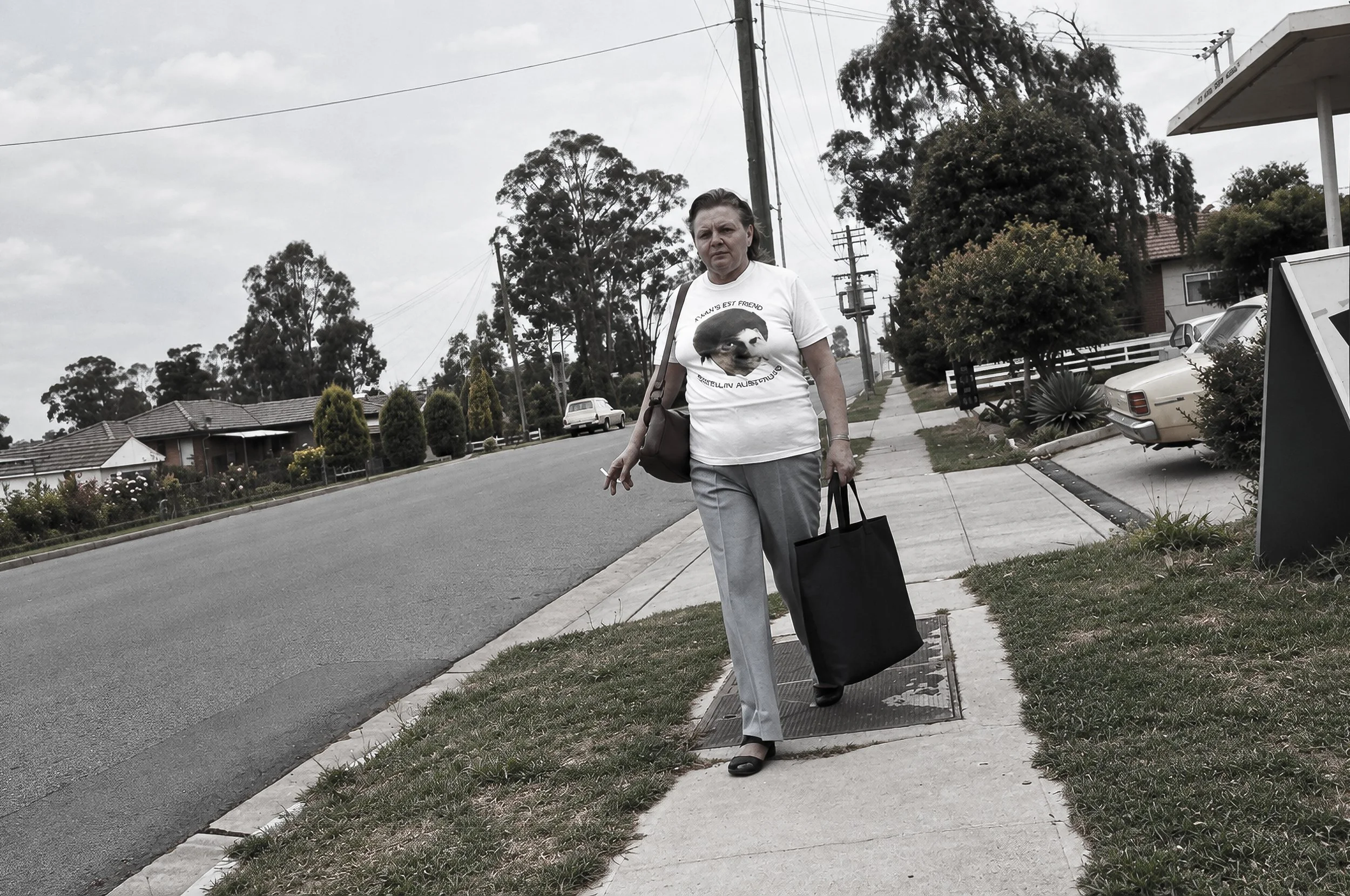 Sydney Suburban Street - A woman walks along a quiet suburban Sydney street carrying shopping bags. Houses, gardens, parked cars and the broad pavement provide a contrasting view of everyday life away from the central city.